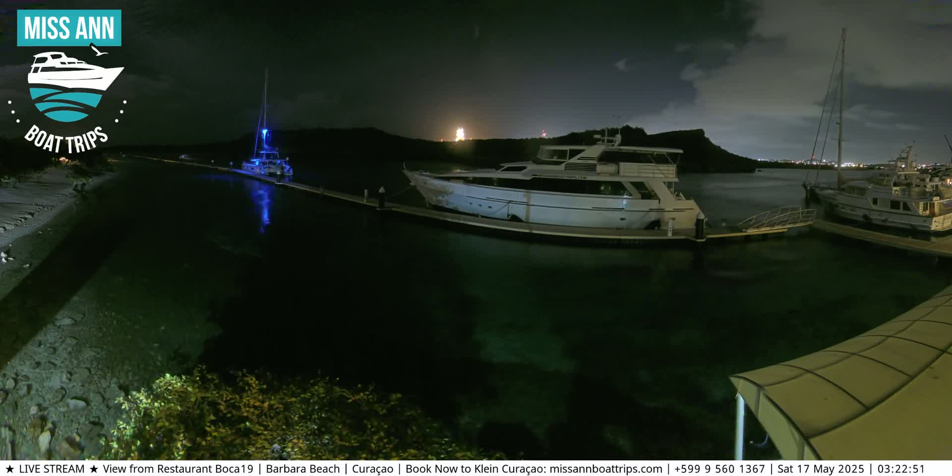 Several yachts are docked at a marina at night under a partly cloudy sky.