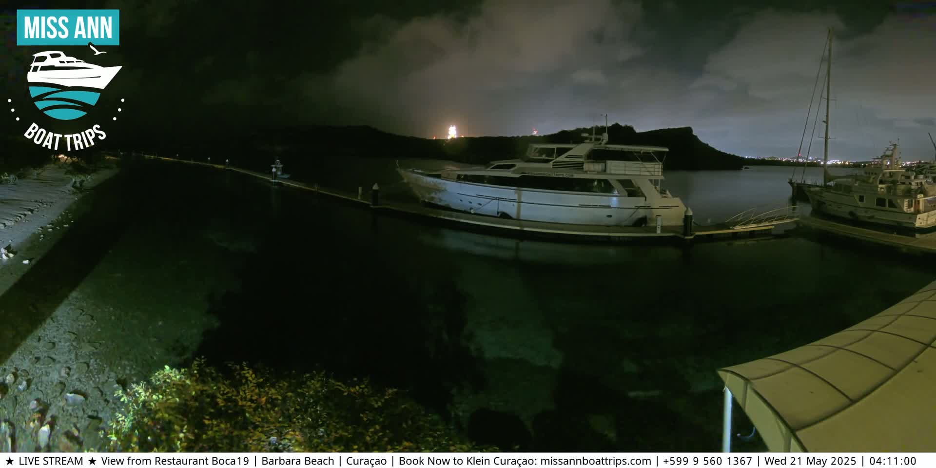 A marina at night under a cloudy sky, with several boats docked and lights visible in the distance.