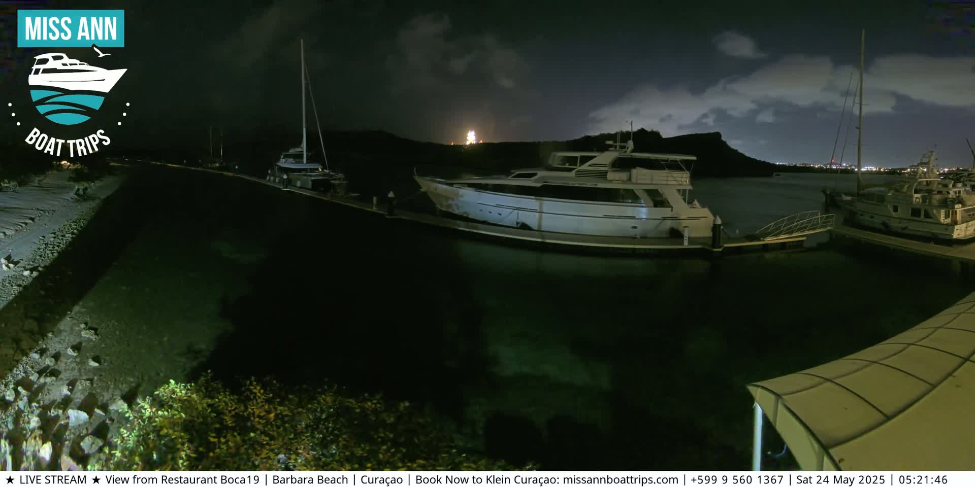 Several boats are docked at a marina at night under a partly cloudy sky.