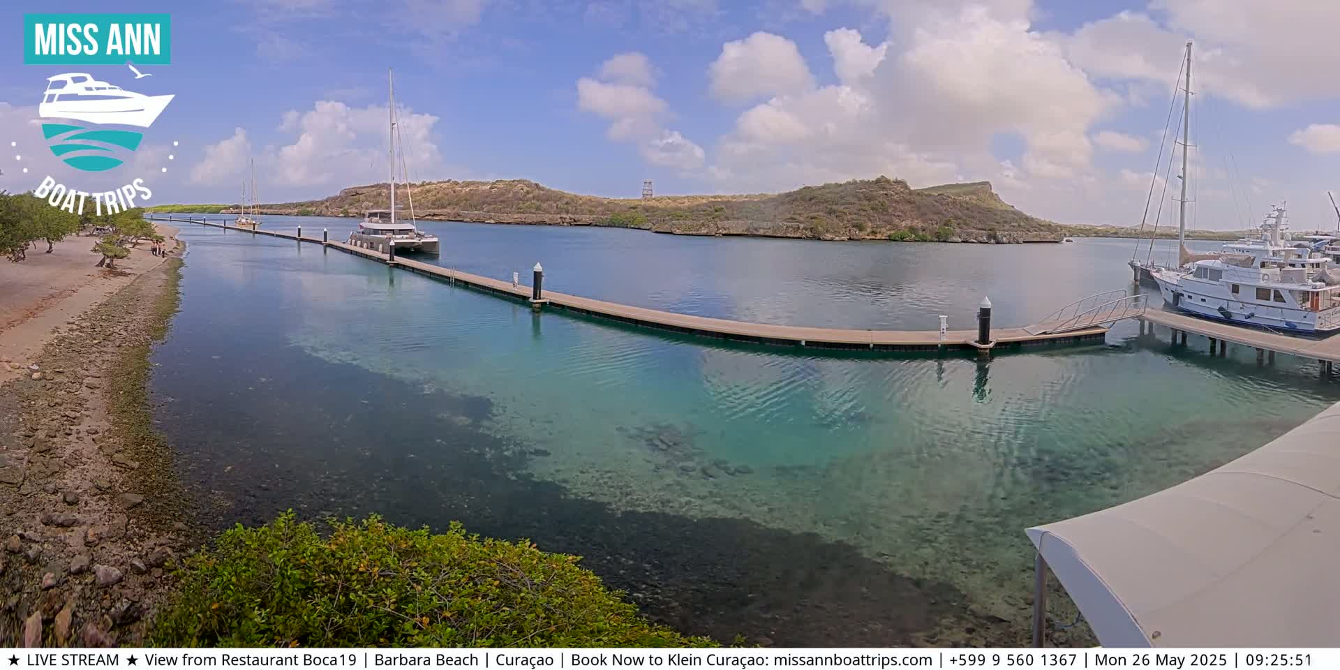 A marina with several boats docked at piers on clear, shallow turquoise water, under a partly cloudy sky.
