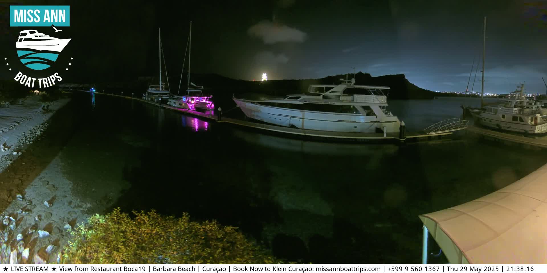Several boats are docked at a marina at night under a partly cloudy sky.