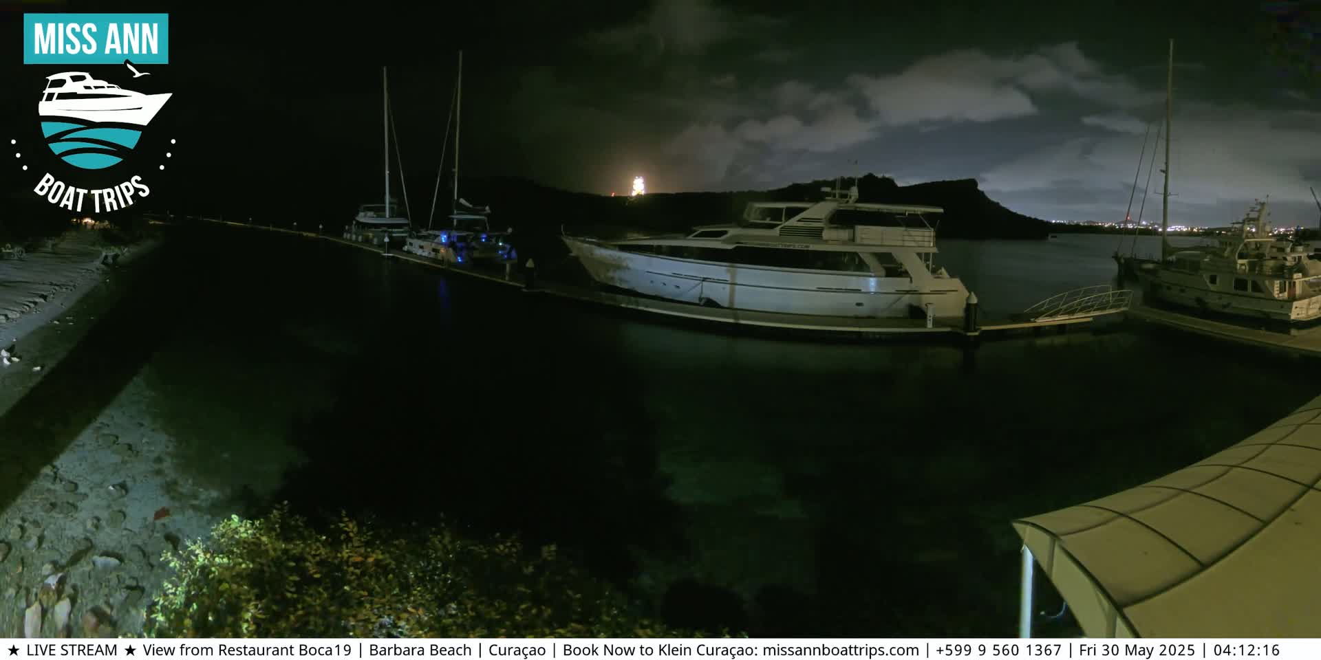 Several boats are moored at a dock at night under a partly cloudy sky.