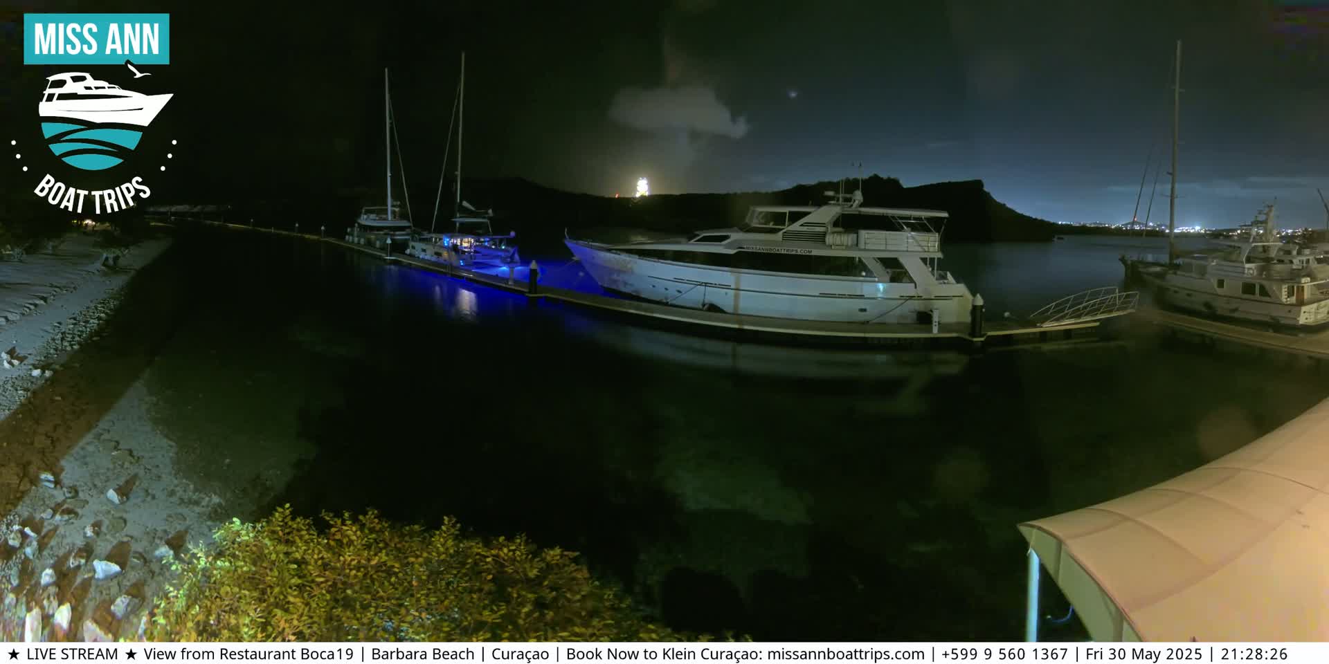 Several yachts are docked at a marina at night under a partly cloudy sky.