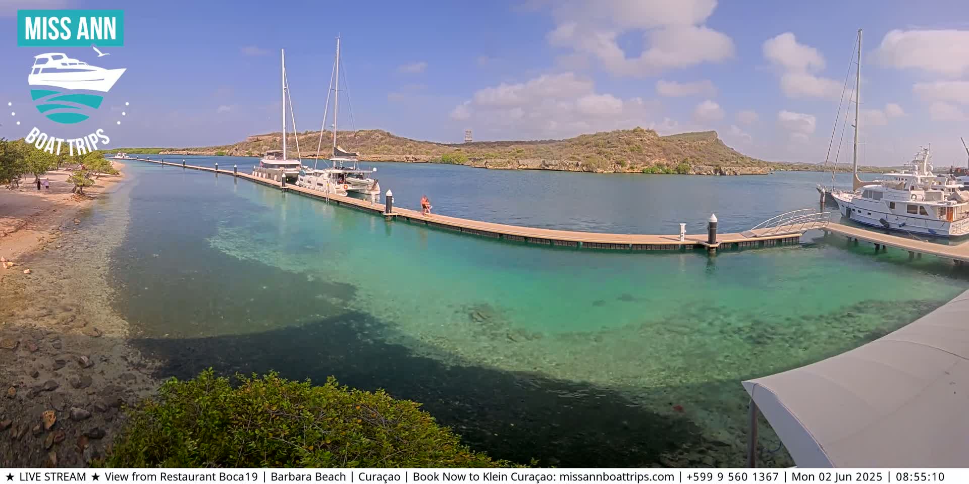 Several boats are docked at a marina on a sunny day with clear, shallow turquoise water.