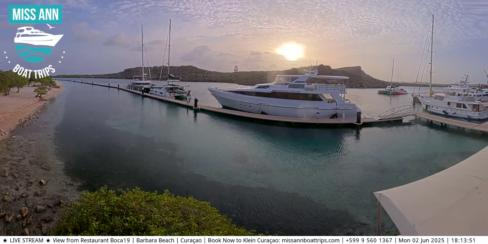 Several boats are moored at a marina at sunset, with calm, clear water visible.