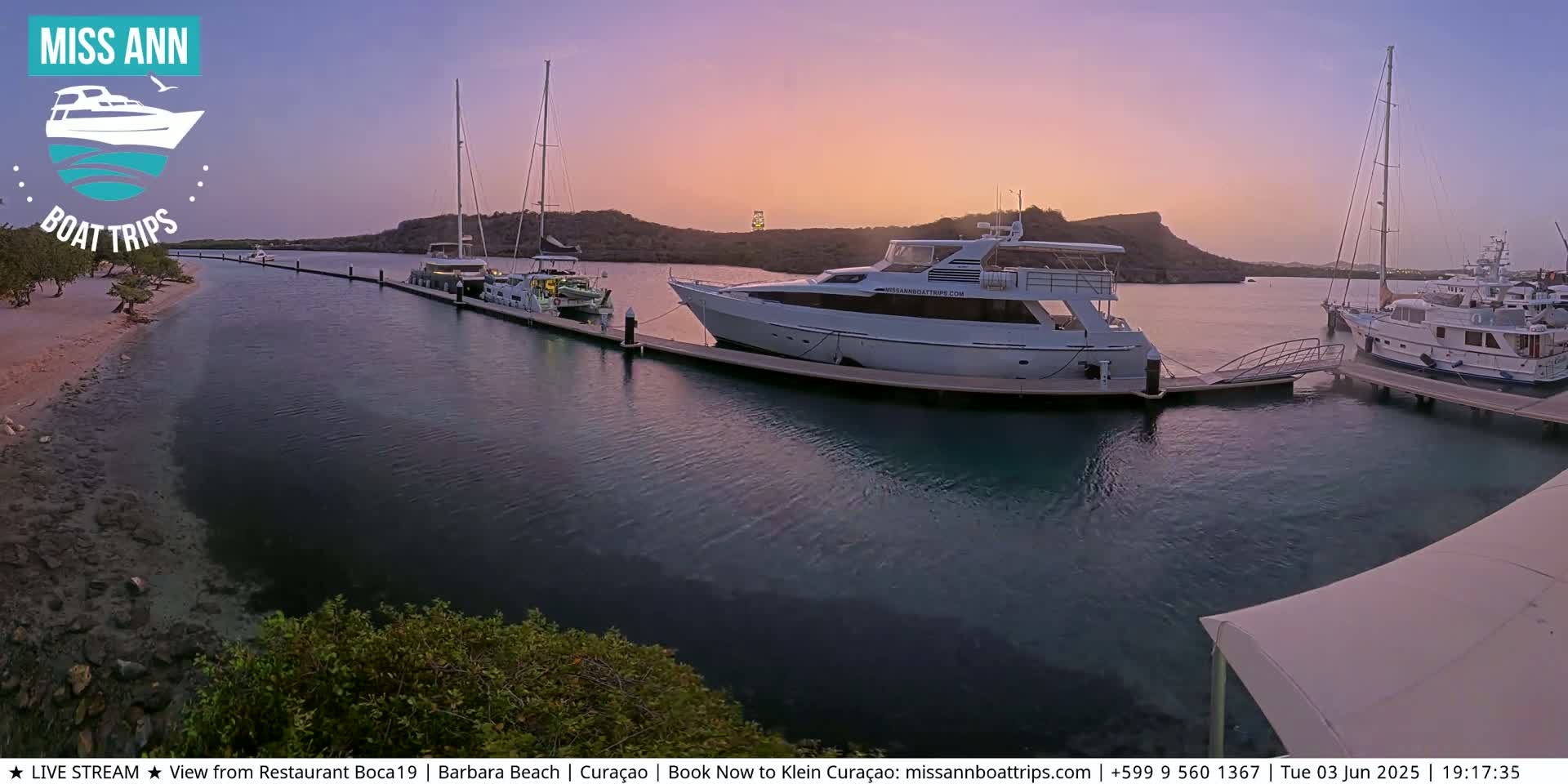 Several yachts are docked at a marina during a calm, sunset hour with a pinkish-purple sky.