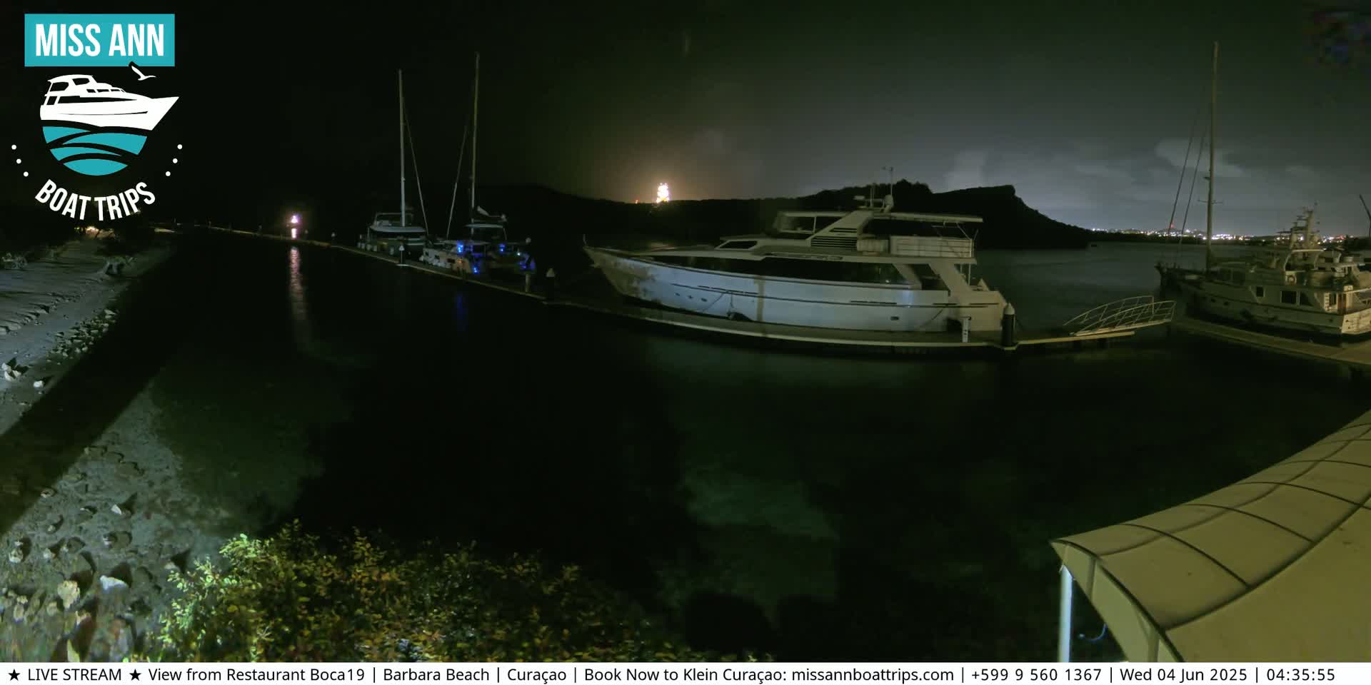 Several boats are docked at a marina at night under a partly cloudy sky.