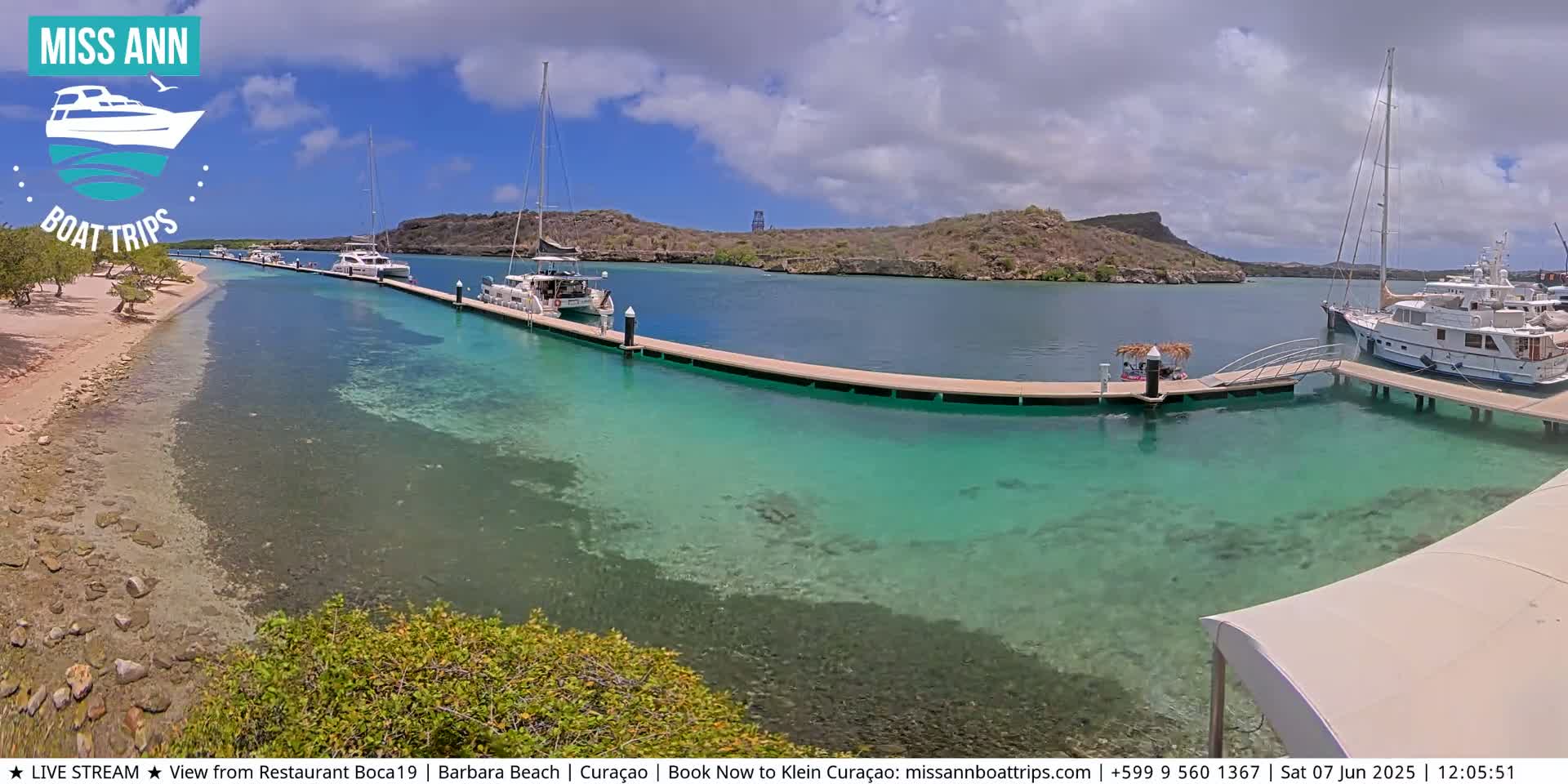 Several boats are docked at a marina on a sunny day with clear, shallow, turquoise water.