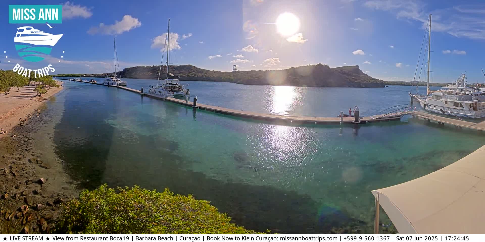 Several boats are docked at a marina on a sunny day with clear, shallow turquoise water.