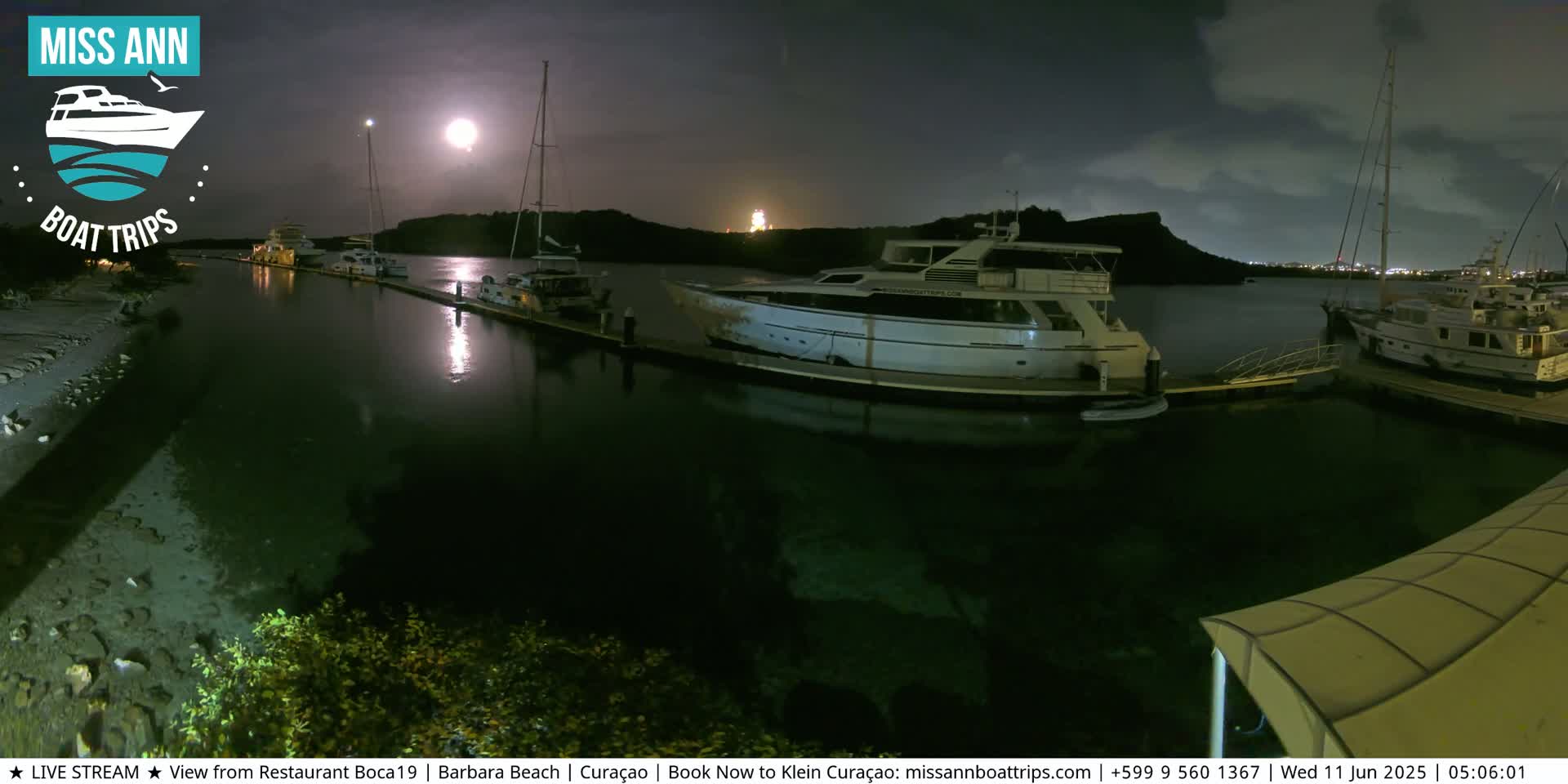 Several yachts are moored at a marina at night under a bright moon and partly cloudy sky.