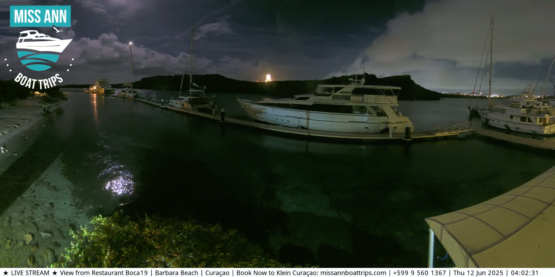 Several yachts are docked at a marina at night under a partly cloudy sky.