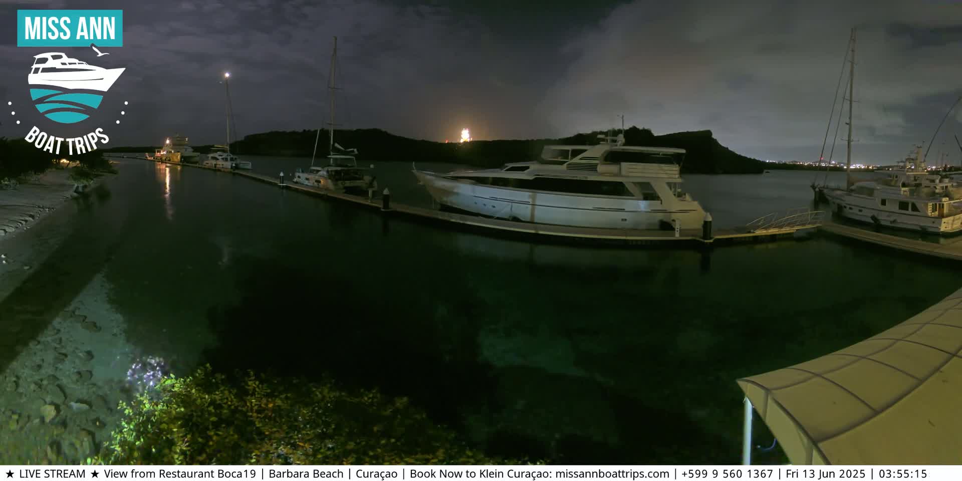 Several yachts are docked at a marina at night under a dark, cloudy sky.