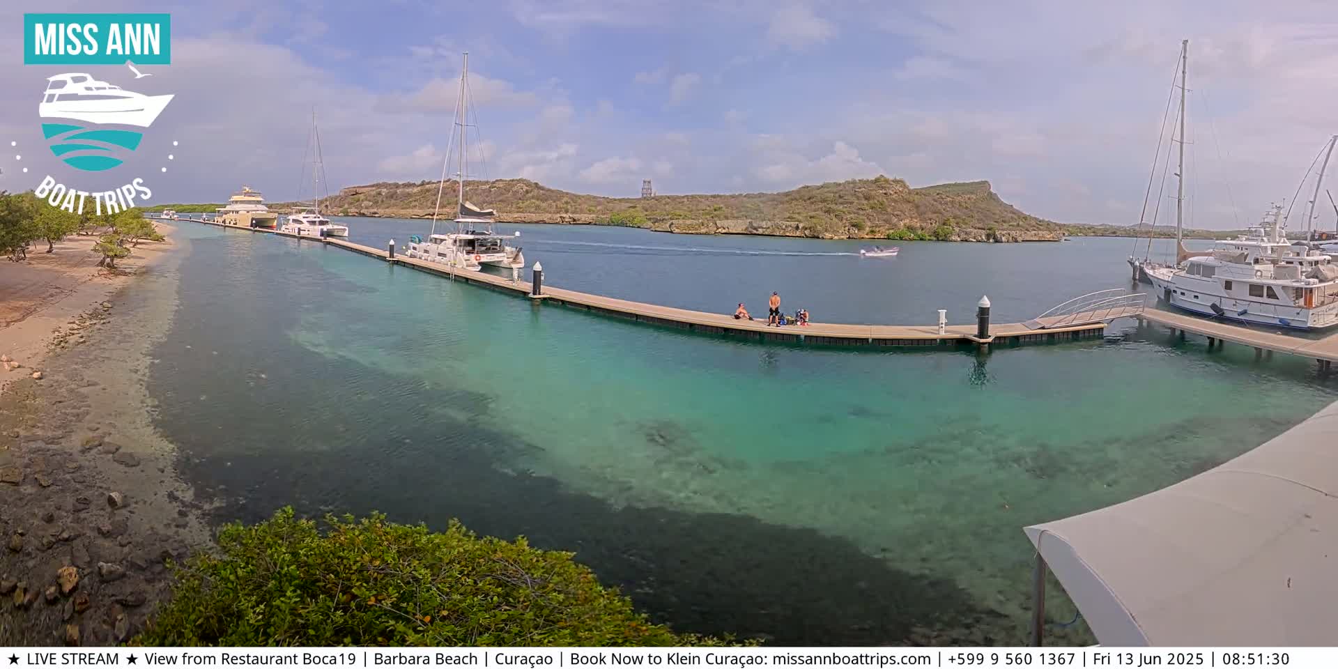 Several boats are docked at a marina with clear, turquoise water, under a mostly sunny sky.