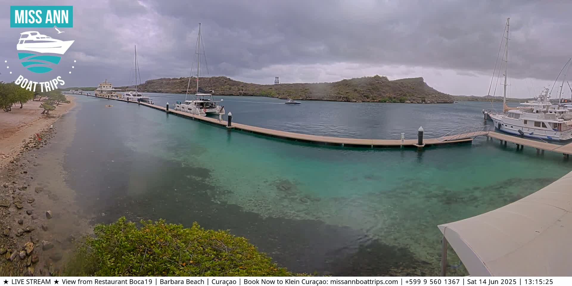 Several boats are docked at a marina with clear, shallow turquoise water, under an overcast sky.