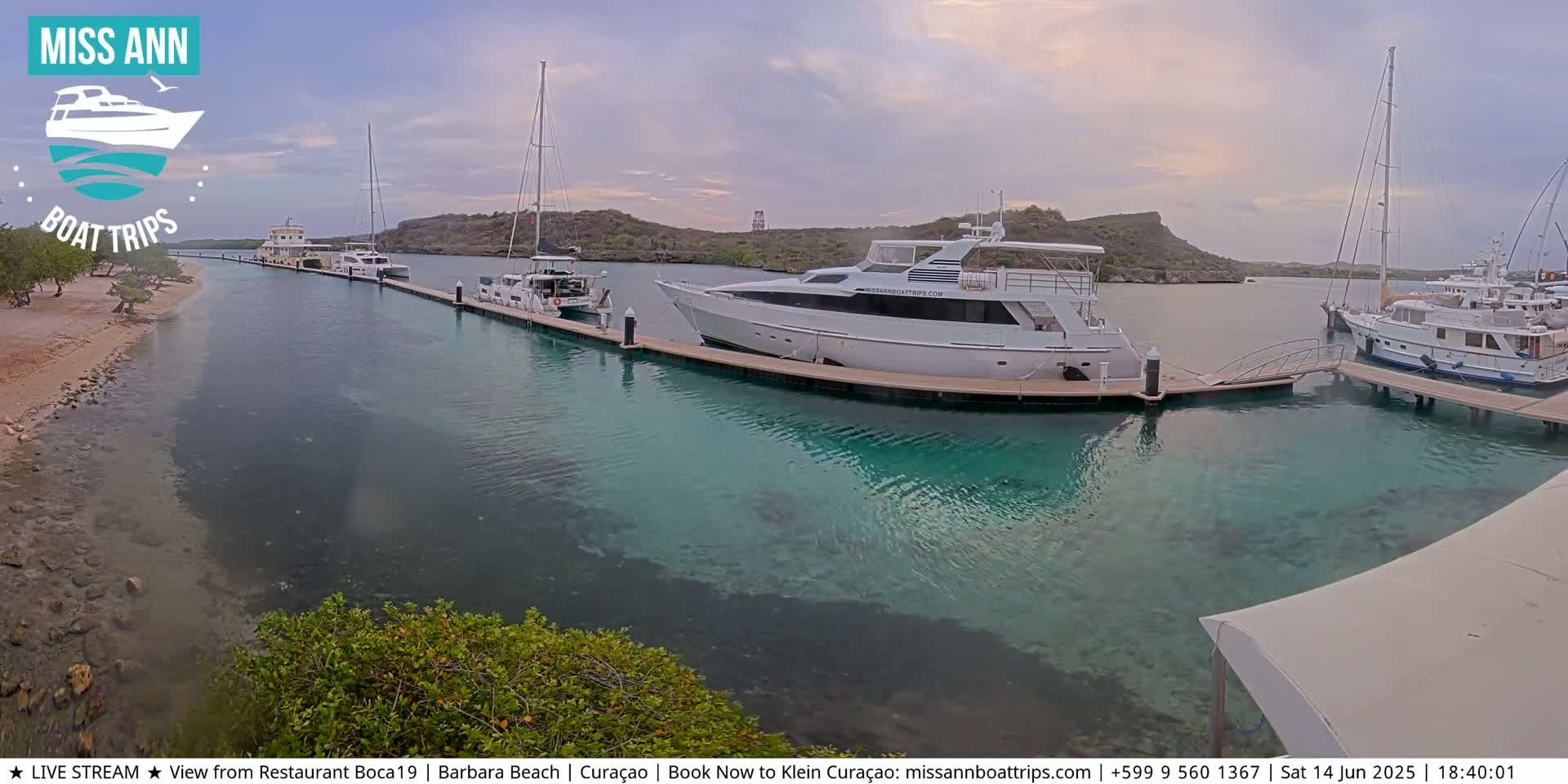 Several boats are docked at a marina with clear, shallow turquoise water, under an overcast sky.