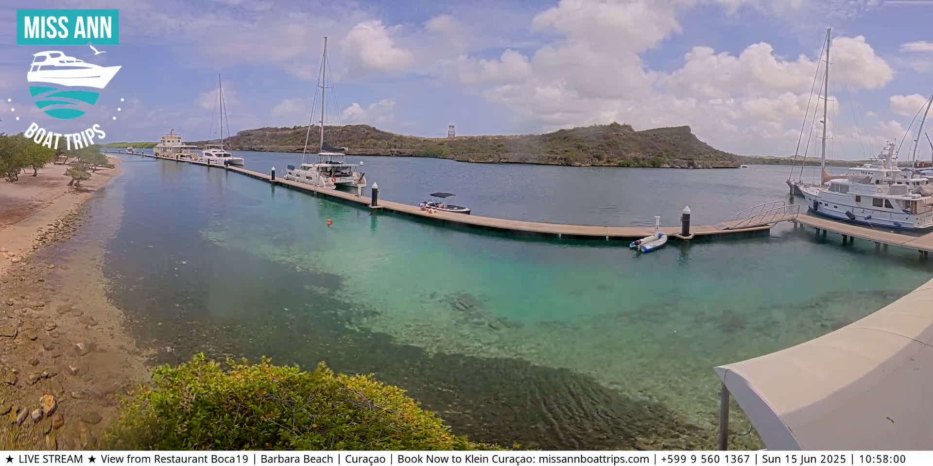 Several boats are docked at a marina on a sunny day with clear, shallow turquoise water.