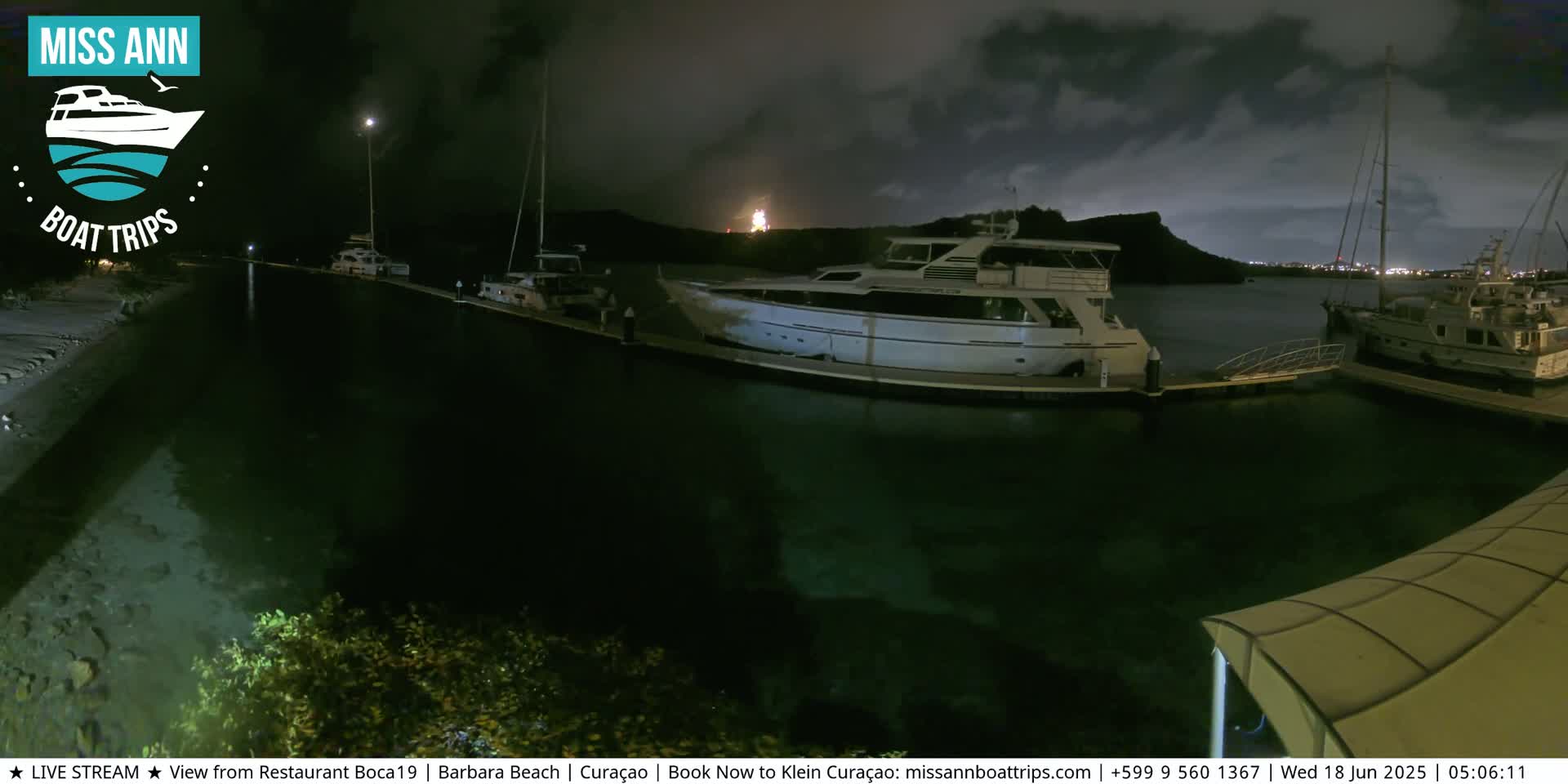 Several boats are docked at a marina at night under a partly cloudy sky.