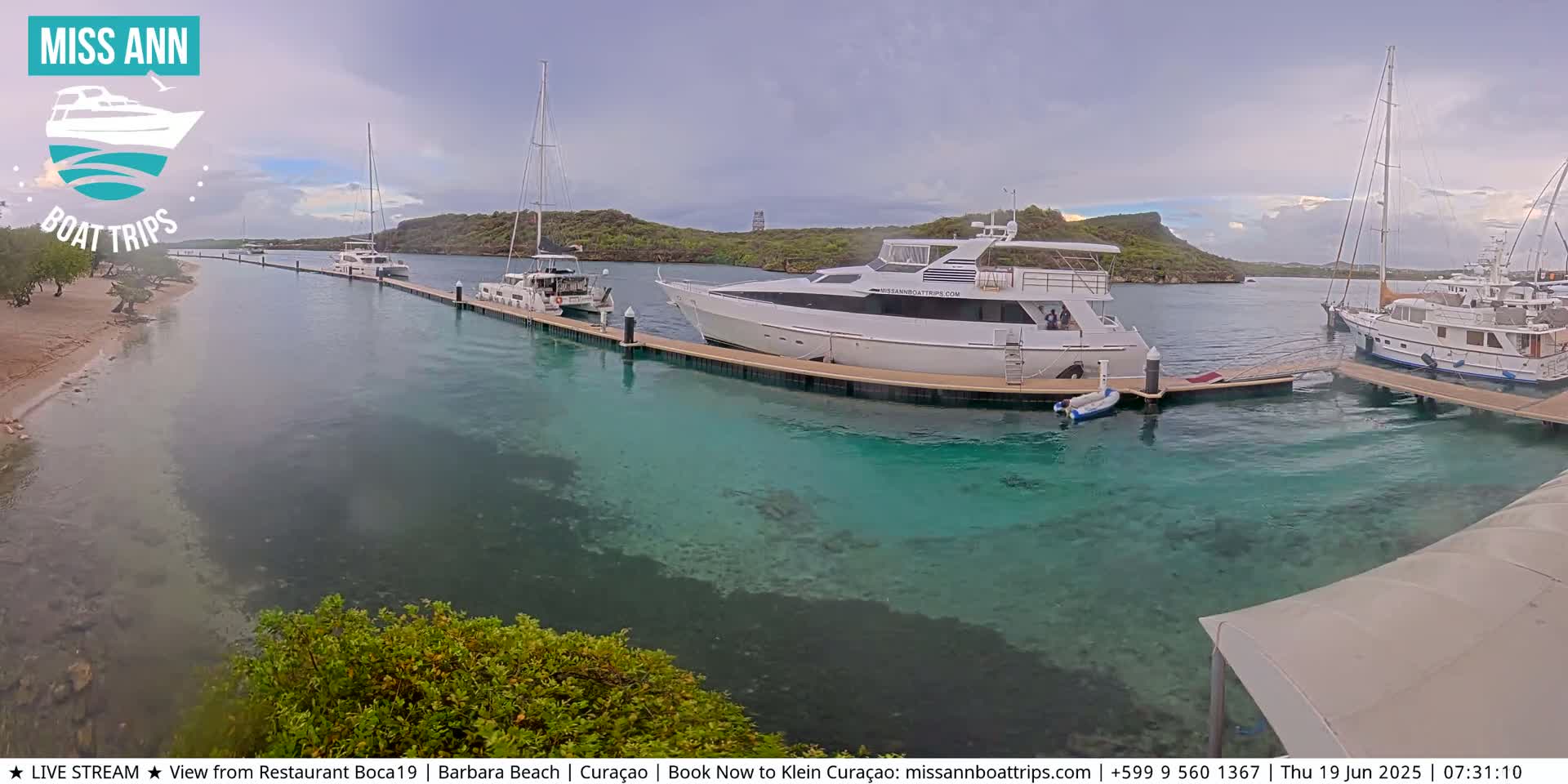 Several boats are docked at a marina with clear, shallow turquoise water, under an overcast sky.