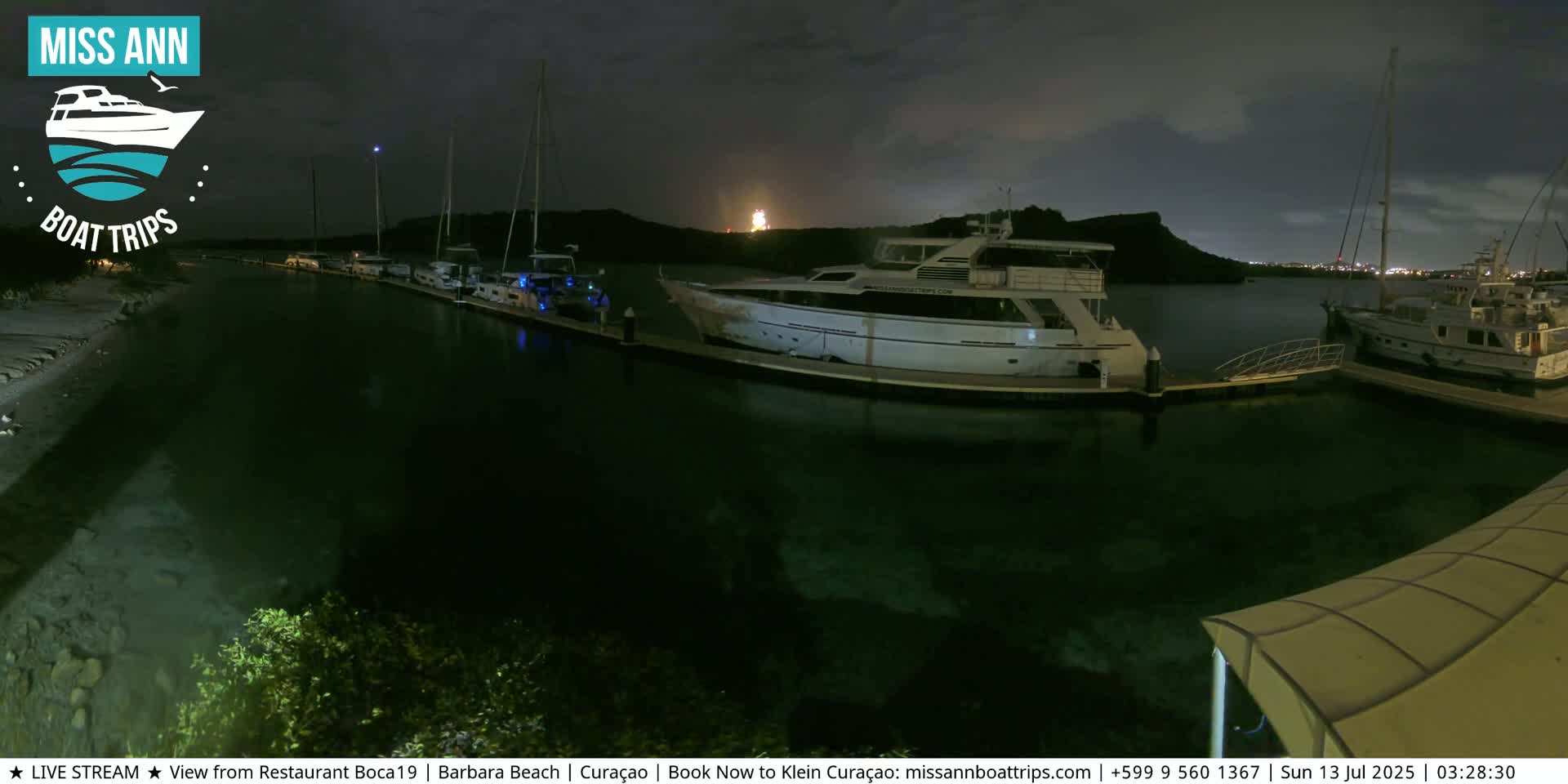 Several boats are docked at a marina at night under a partly cloudy sky.