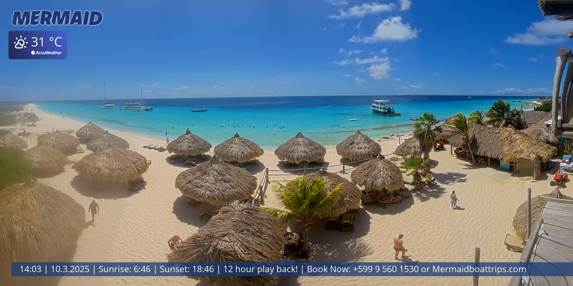 A sunny beach with turquoise water, numerous thatched-roof huts, and several boats offshore.