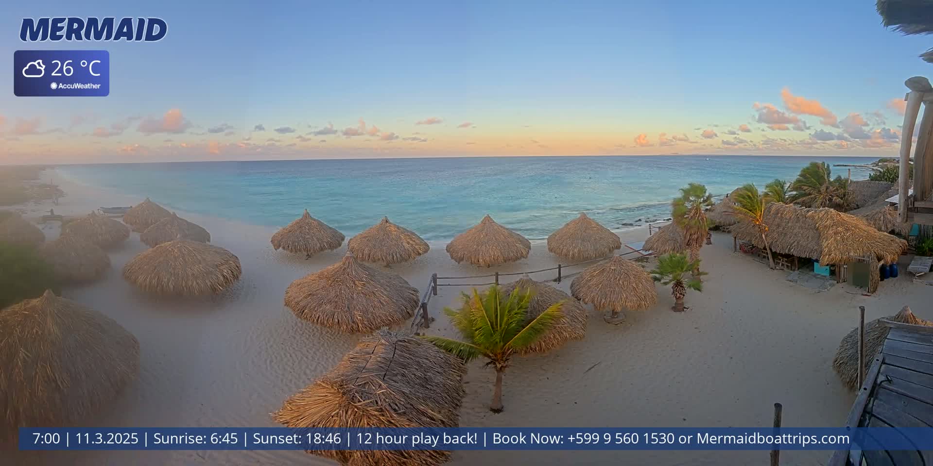 A sandy beach with numerous thatched umbrellas overlooks a calm, turquoise ocean under a partly cloudy, sunset sky.