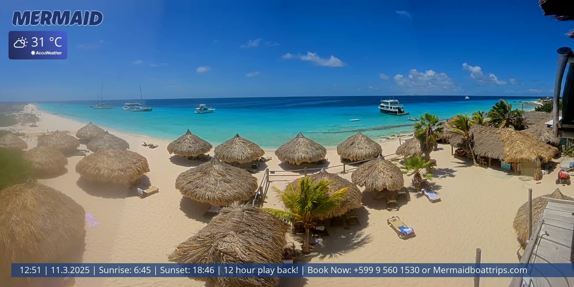 A sunny beach with turquoise water, numerous thatched-roof huts, and several boats offshore.