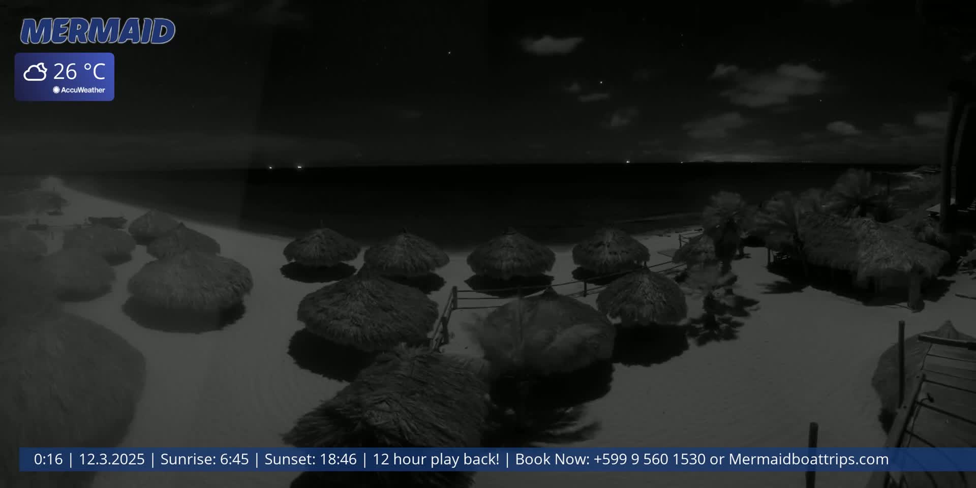 A nighttime beach scene with several thatched umbrellas on the sand, a calm sea, and a partly cloudy sky.