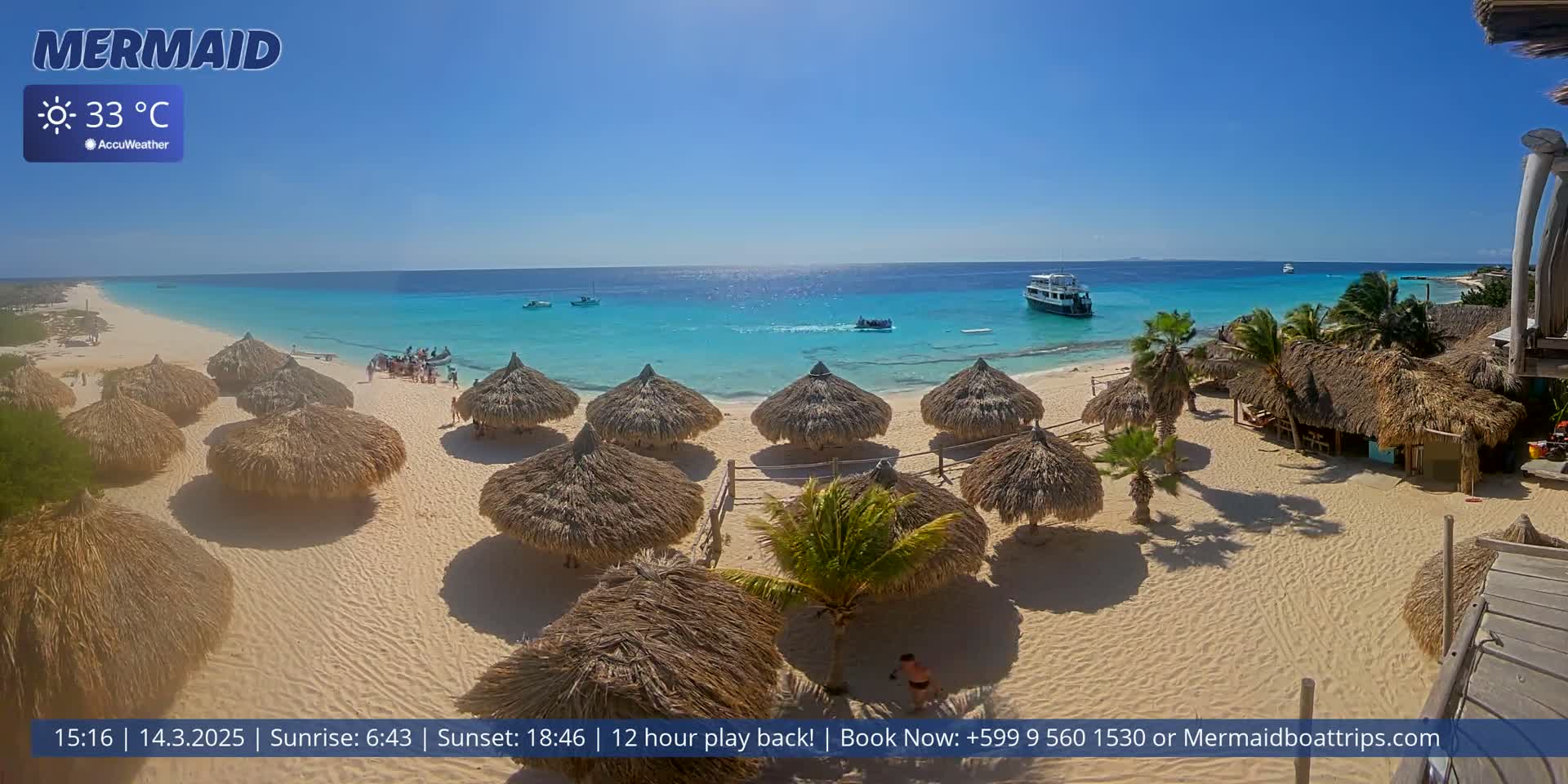 A sunny beach scene with turquoise water, numerous thatched-roof beach umbrellas, and a few boats offshore.