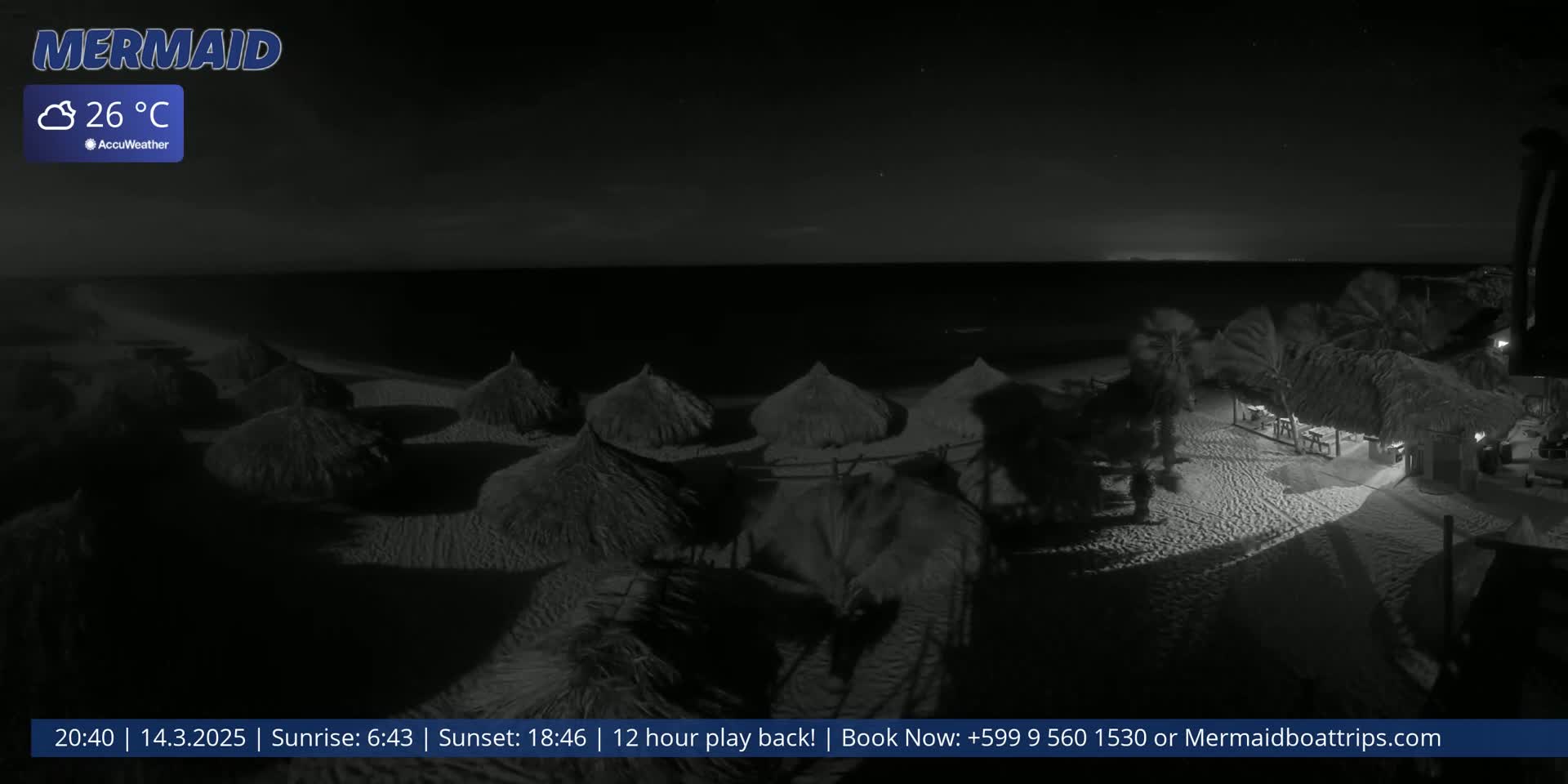 A nighttime beach scene shows several thatched-roof structures on a sandy shore, with palm trees and a calm ocean under a clear, dark sky at 26°C.