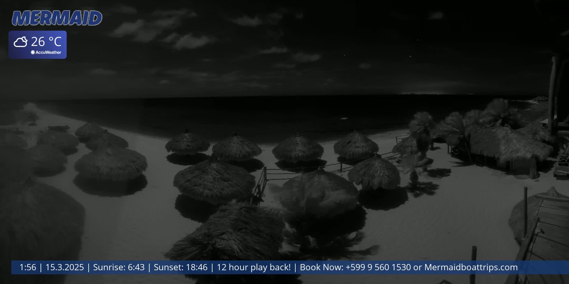 A nighttime beach scene shows several thatched-roof beach umbrellas on a sandy shore under a partly cloudy sky, with a calm ocean in the background.
