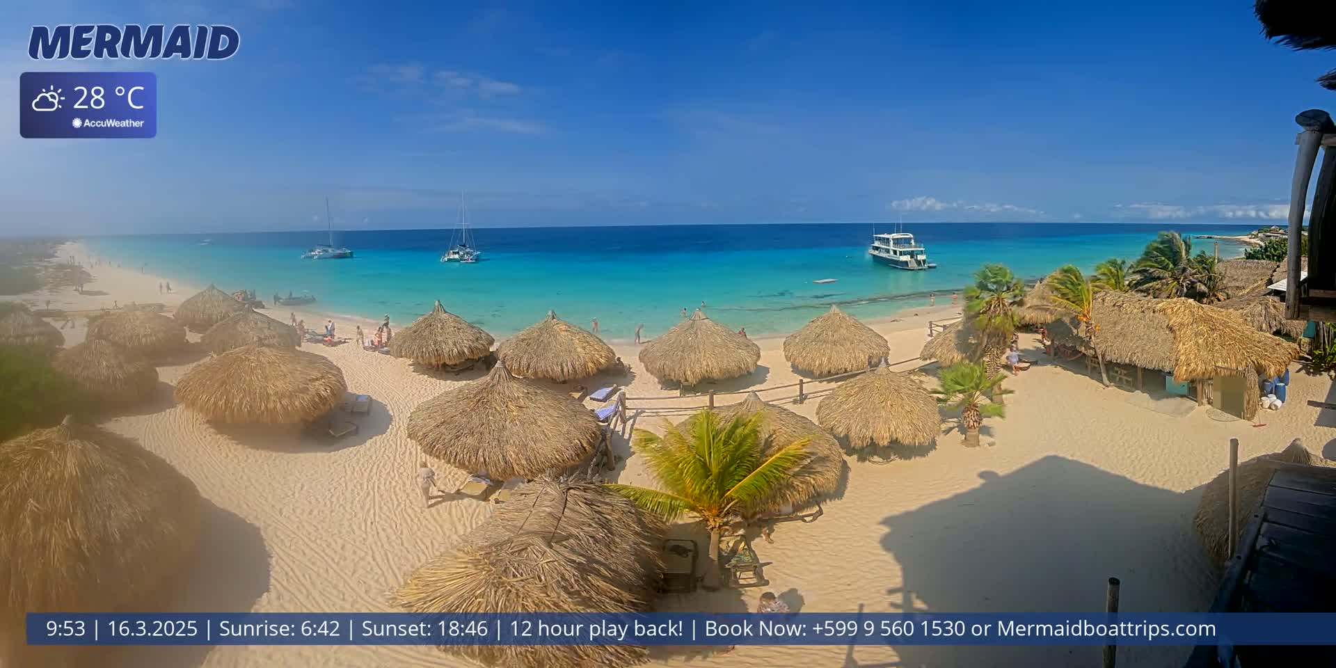 A beach with numerous thatched-roof structures, a few boats offshore, and clear turquoise water under a bright sunny sky.