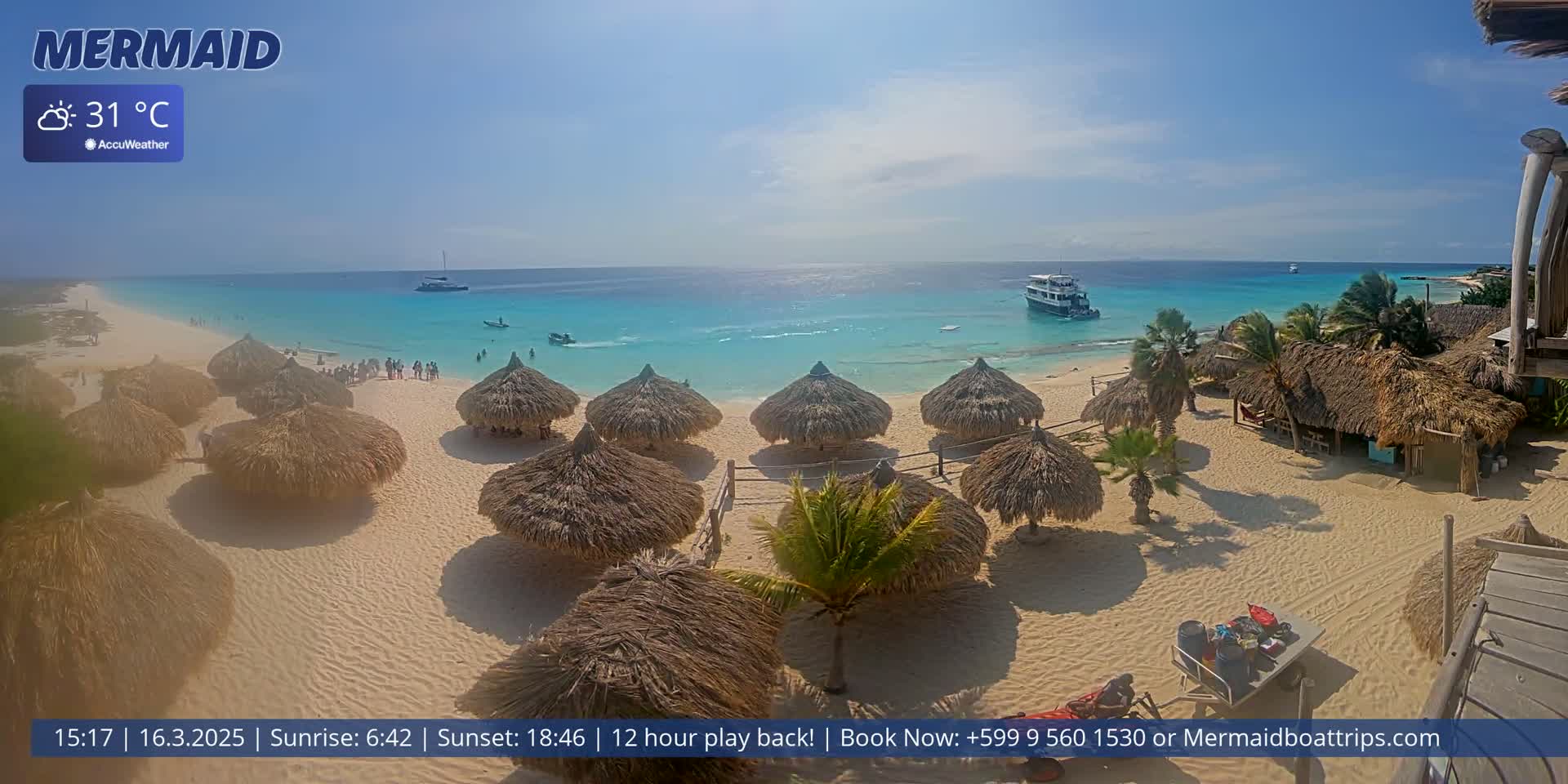A sandy beach with numerous thatched-roof huts is shown, overlooking turquoise water on a sunny day, with a boat visible in the distance.