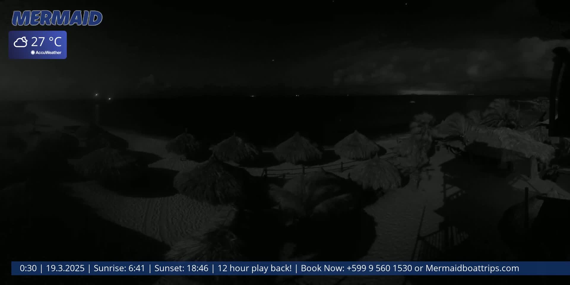A nighttime beach scene shows several thatched-roof beach umbrellas on a sandy shore under a cloudy sky, with a calm ocean visible in the background.