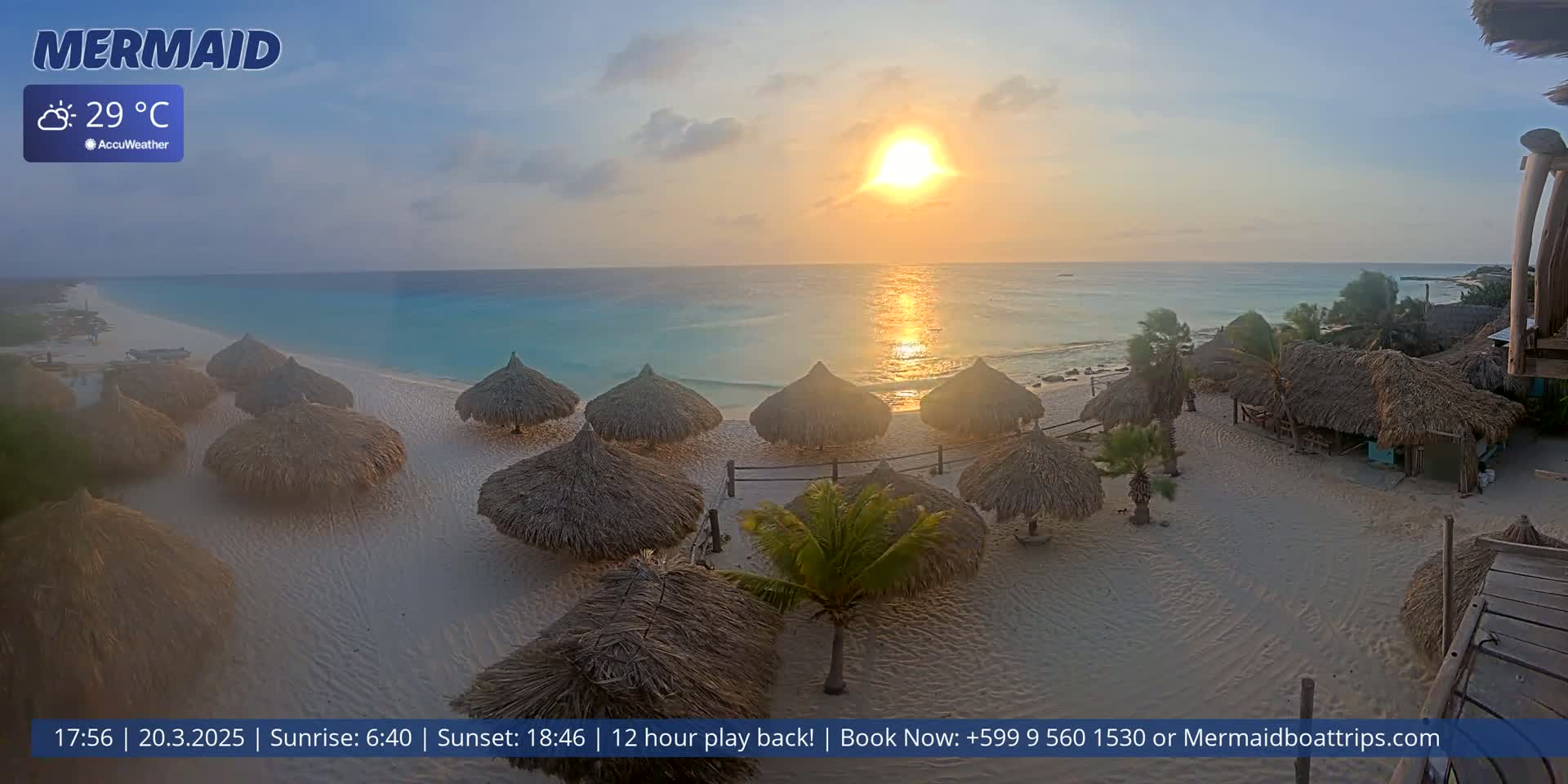 A beach with numerous thatched-roof umbrellas at sunset, under partly cloudy skies and a temperature of 29°C.