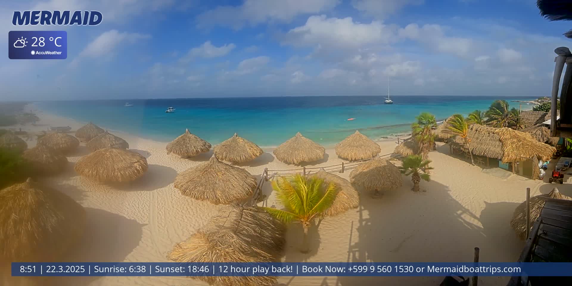 A sandy beach with numerous thatched-roof huts is shown, overlooking a calm, turquoise ocean under a partly cloudy sky; the temperature is 28°C.