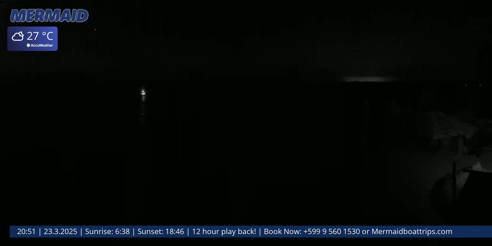 A dark nighttime scene shows a body of water with a faint light source in the distance, under a clear sky.