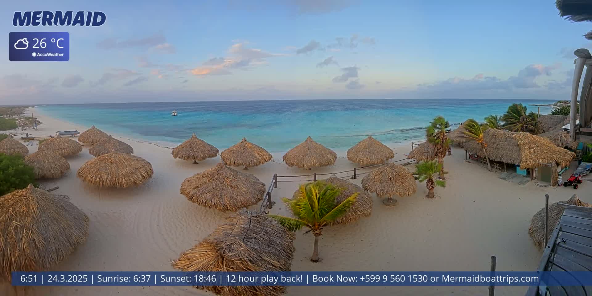 A sandy beach with numerous thatched umbrellas overlooks a calm, turquoise ocean under a partly cloudy sky.