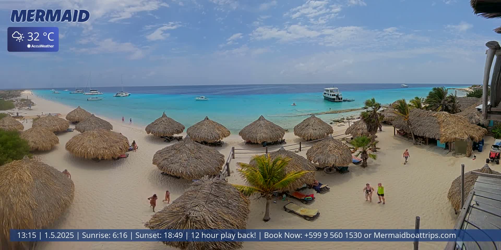 A beach with numerous thatched-roof huts, several boats in the turquoise water, and a few people scattered on the sand under mostly sunny skies.
