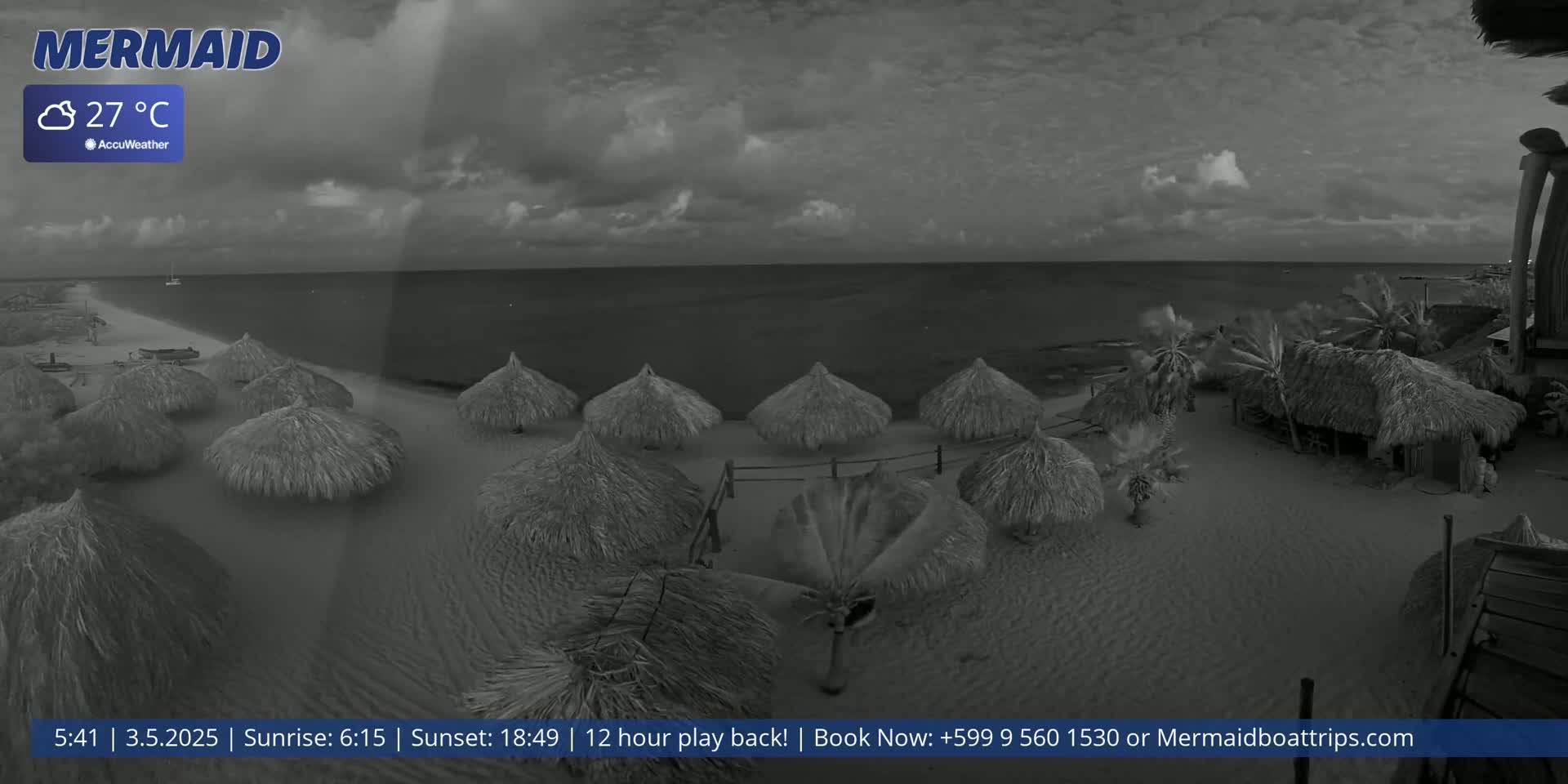 A beach scene under a cloudy sky shows numerous thatch umbrellas on a sandy beach next to a calm sea.
