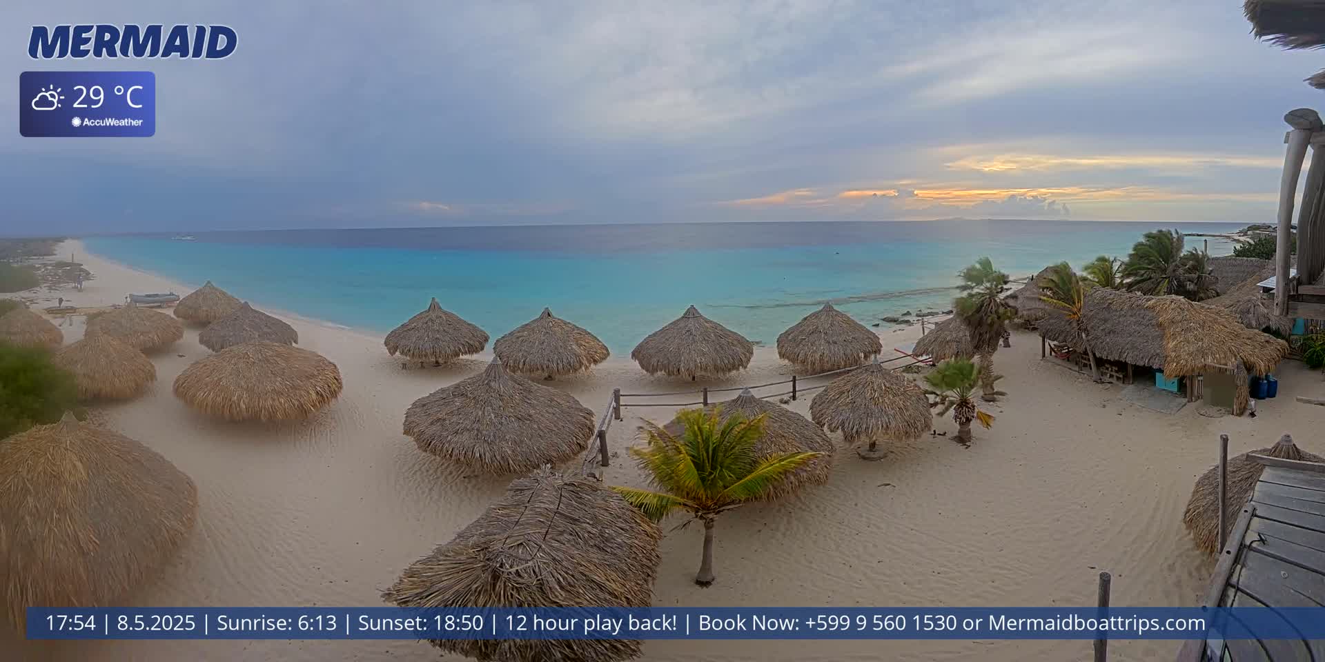 A beach with numerous thatched umbrellas under an overcast sky, featuring calm turquoise water.