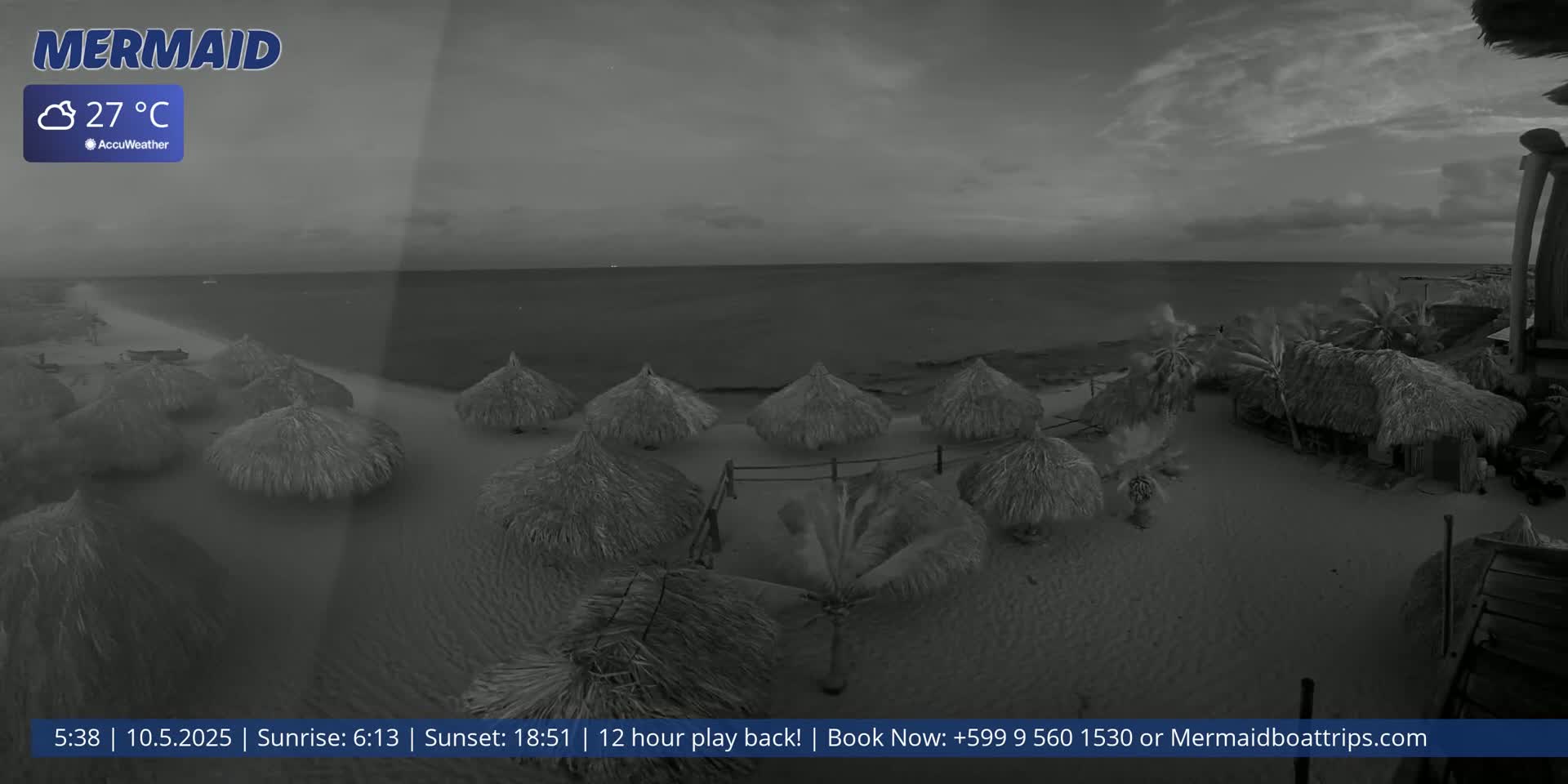 A beach scene at dusk shows numerous thatched umbrellas on a sandy beach next to a calm sea under a cloudy sky.