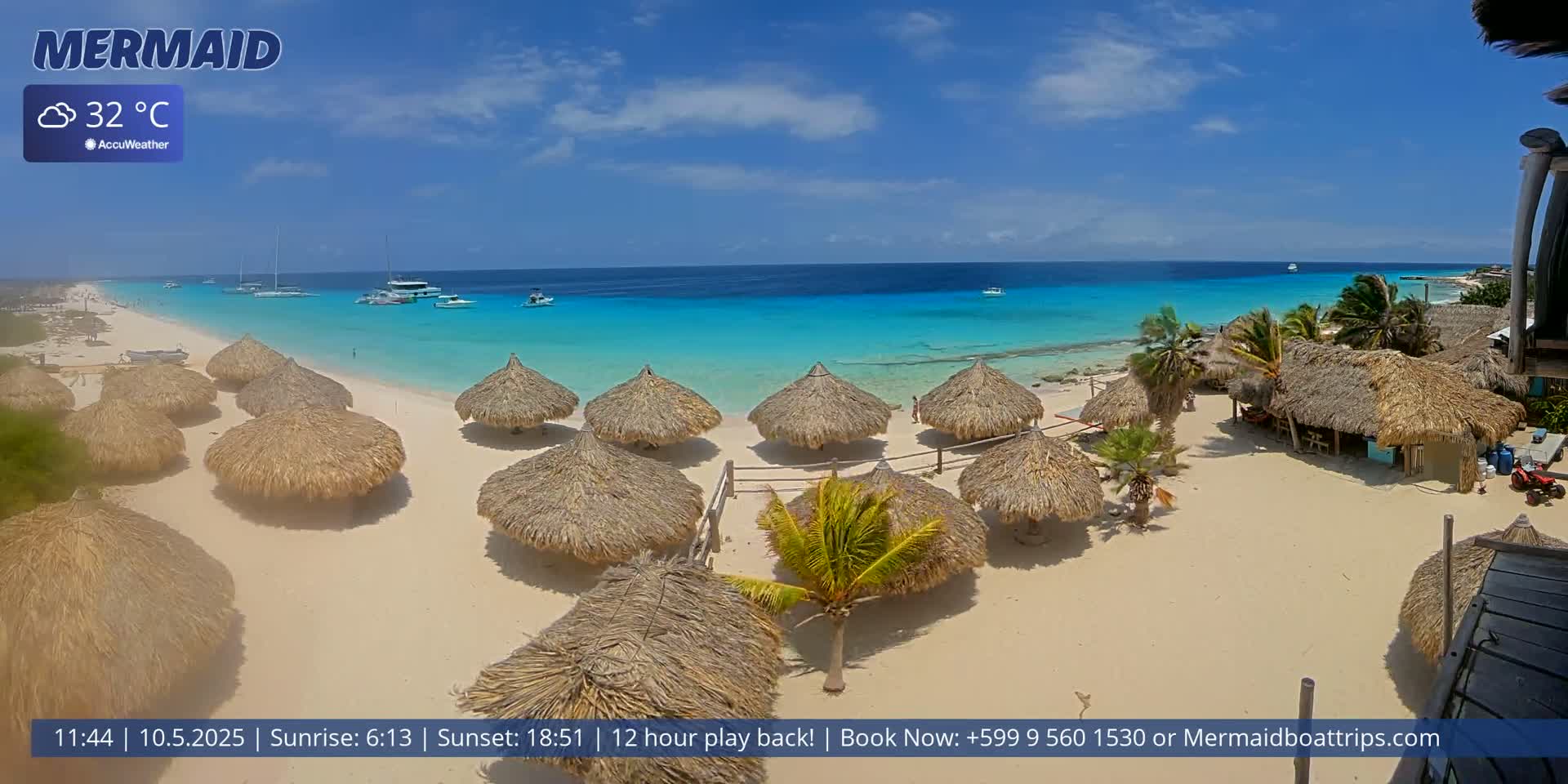 A sandy beach with numerous thatched-roof umbrellas overlooks a calm, turquoise ocean under a sunny sky.