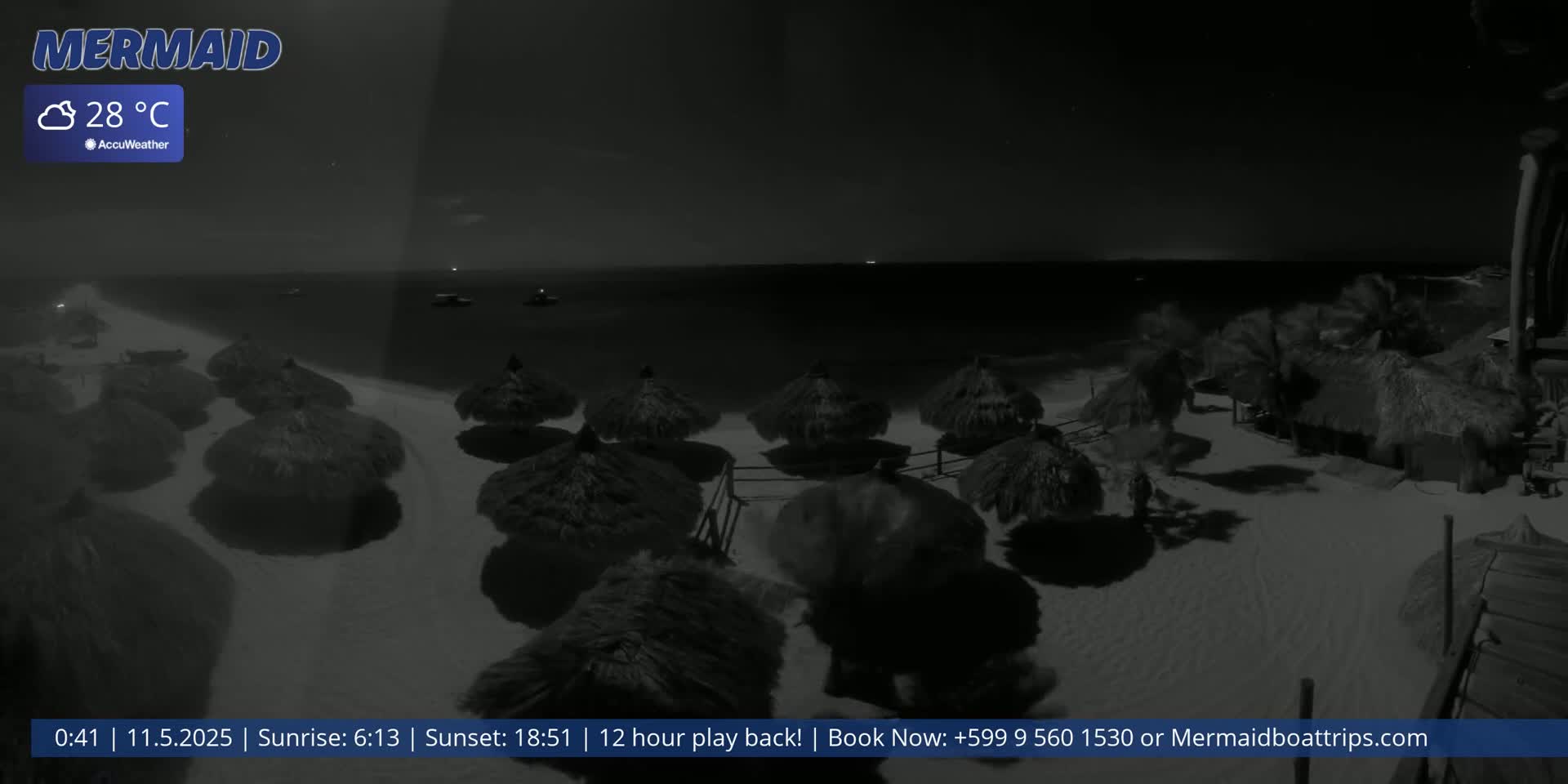 A nighttime beach scene shows numerous thatched umbrellas on a sandy beach, with calm water and a dark sky visible in the background under a 28°C temperature.