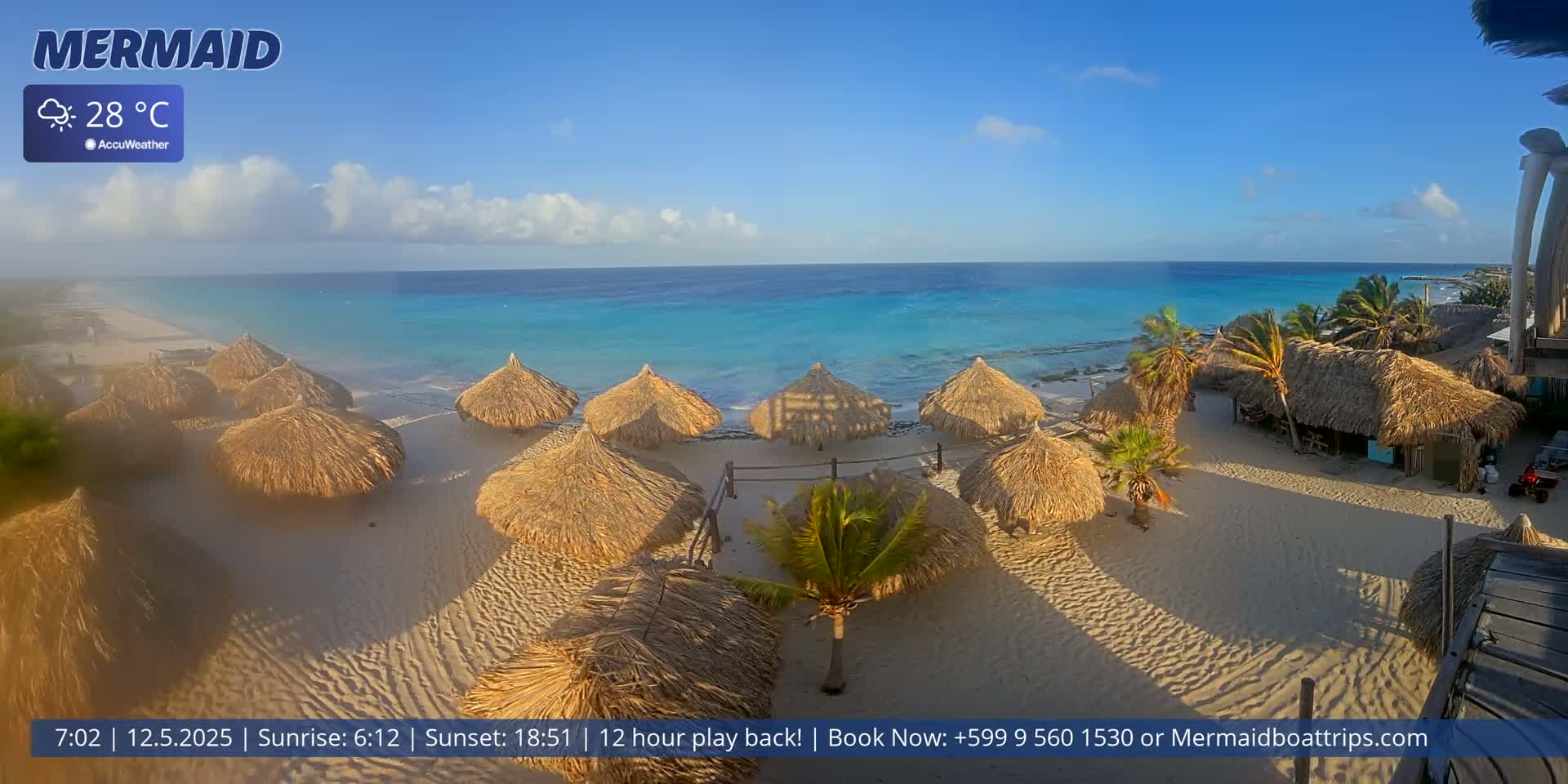 A sandy beach with numerous thatched-roof umbrellas is situated next to a calm, turquoise ocean under a mostly sunny sky.