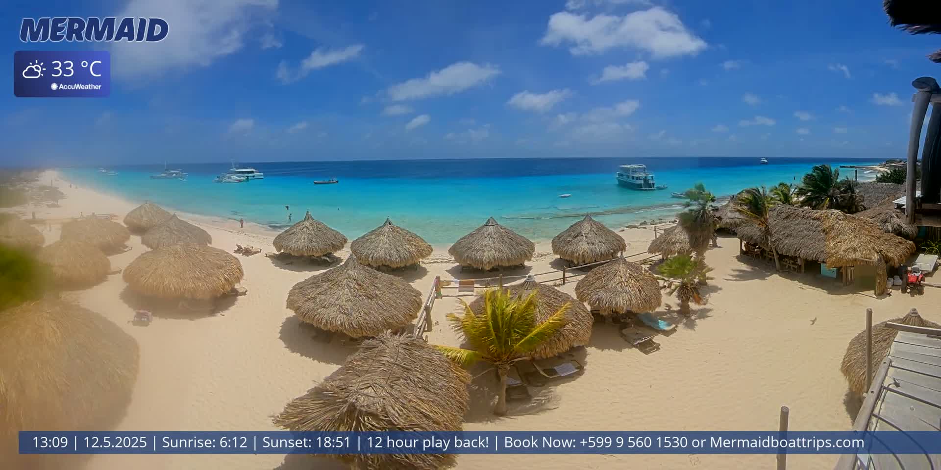 A sunny beach with turquoise water, several thatched-roof huts, and a few boats offshore.