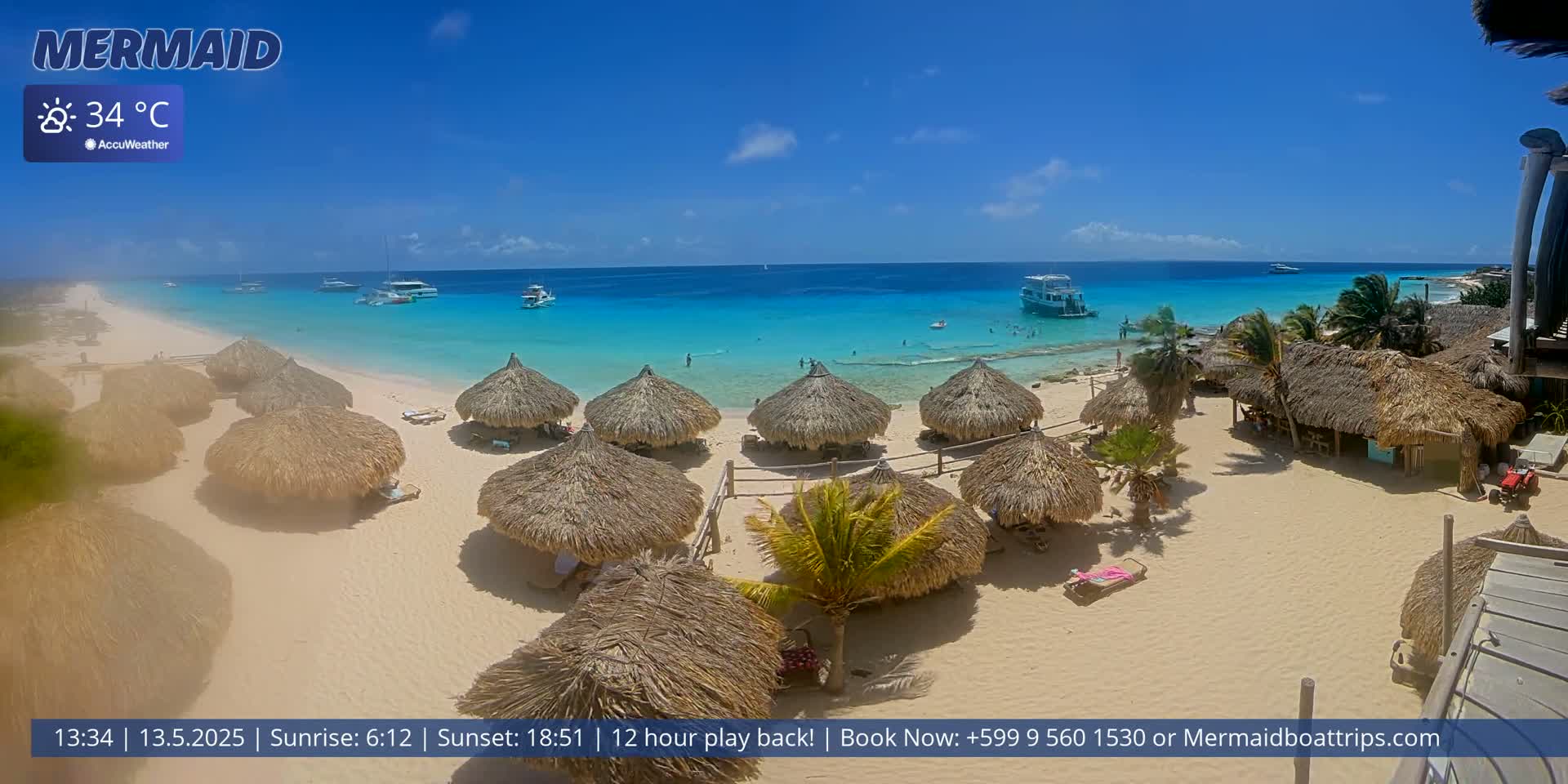 A sandy beach with numerous thatched-roof huts is shown, overlooking a clear turquoise ocean under a sunny sky.