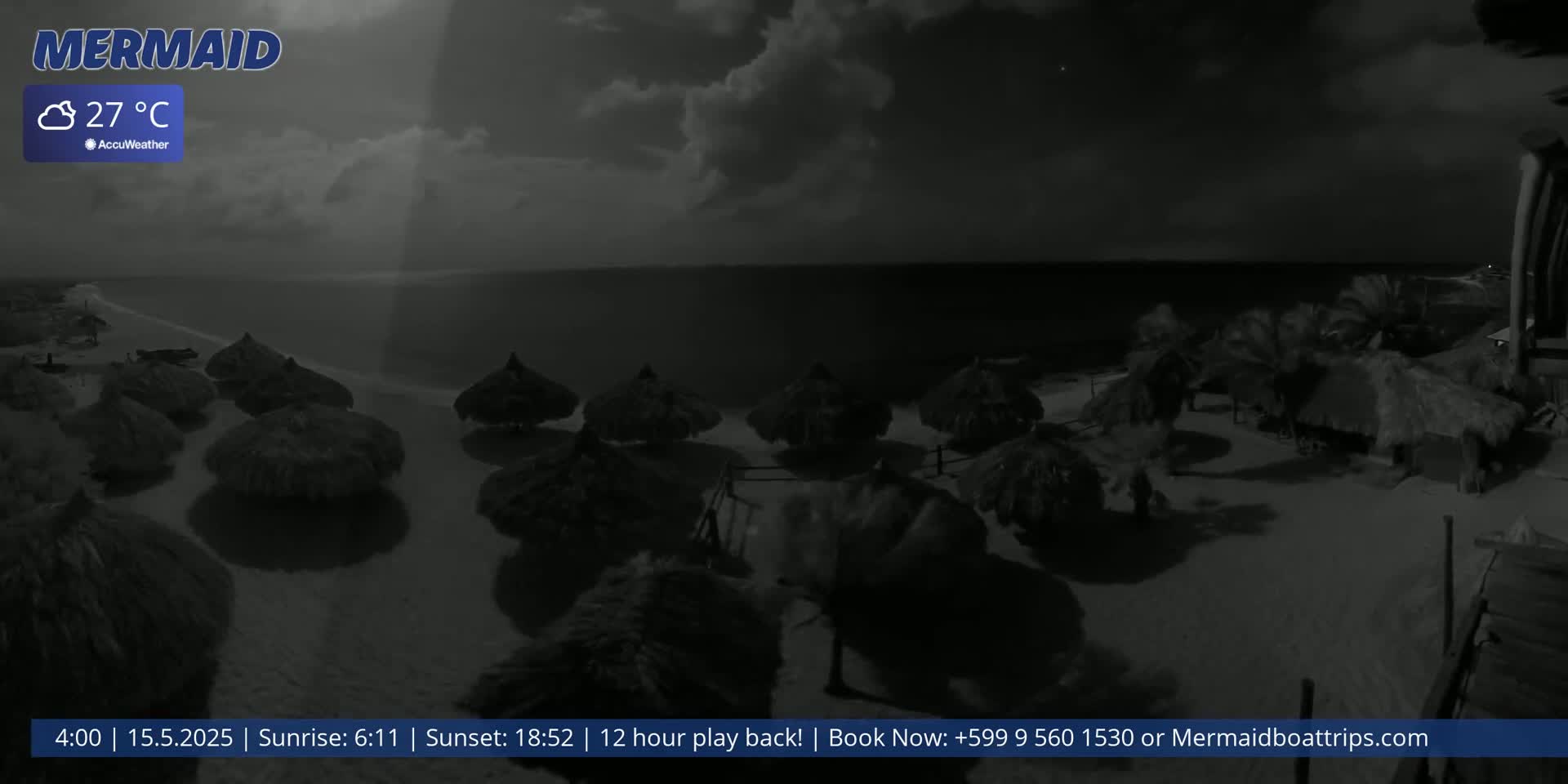 A nighttime beach scene with cloudy skies shows numerous thatched umbrellas on the sand near a calm ocean.
