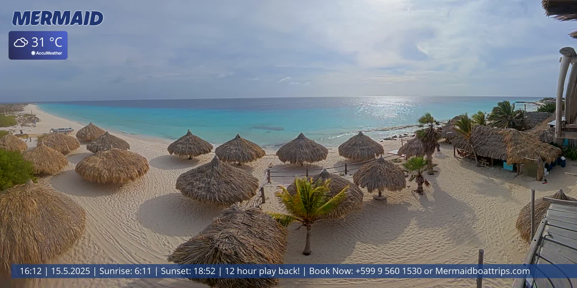 A partly cloudy, sunny beach scene with turquoise water, numerous thatched-roof beach umbrellas, and palm trees on a sandy shore.