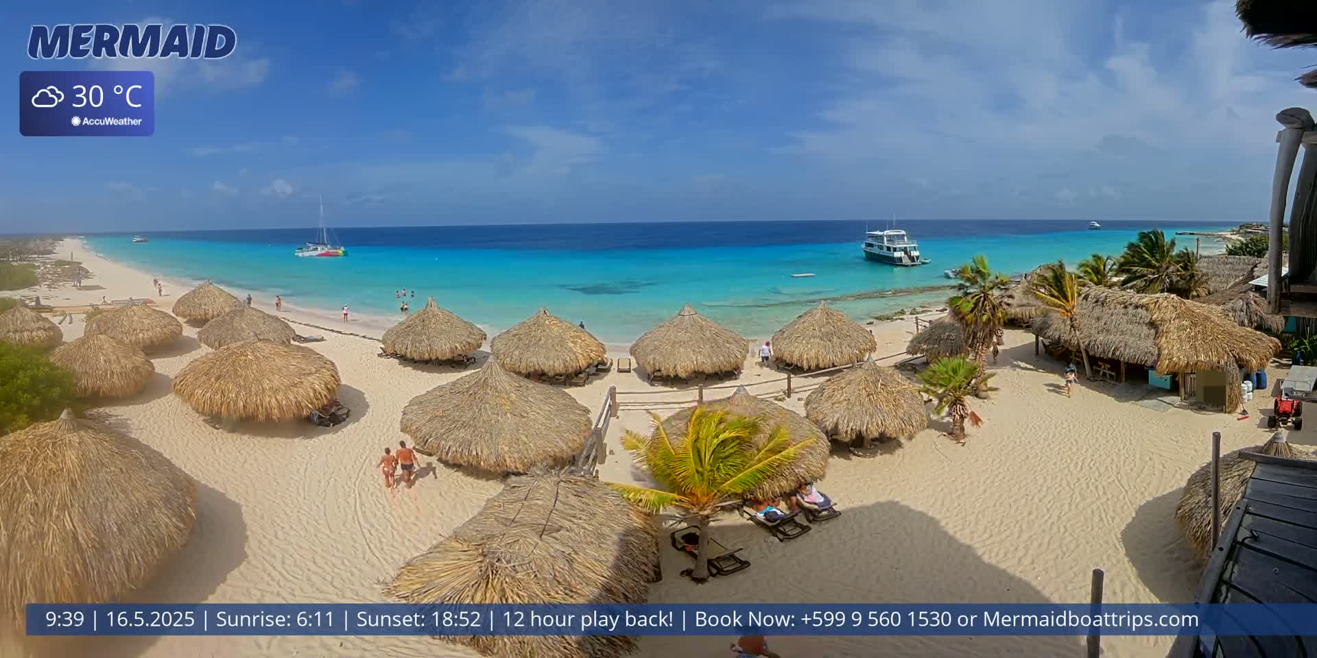 A beach with numerous thatched-roof umbrellas, a few people, and boats offshore on a clear, sunny day with a temperature of 30°C.