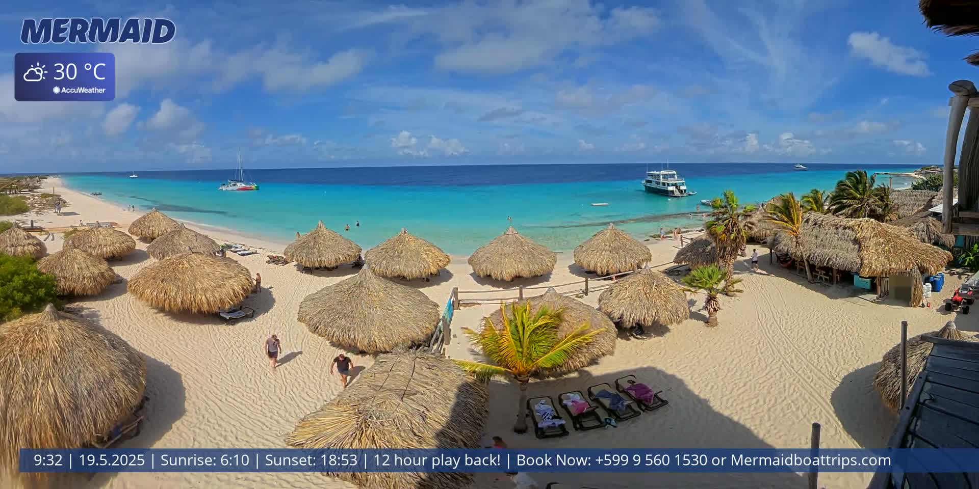 A beach with numerous thatched-roof huts, a few people, and a boat in the turquoise ocean under a sunny sky.
